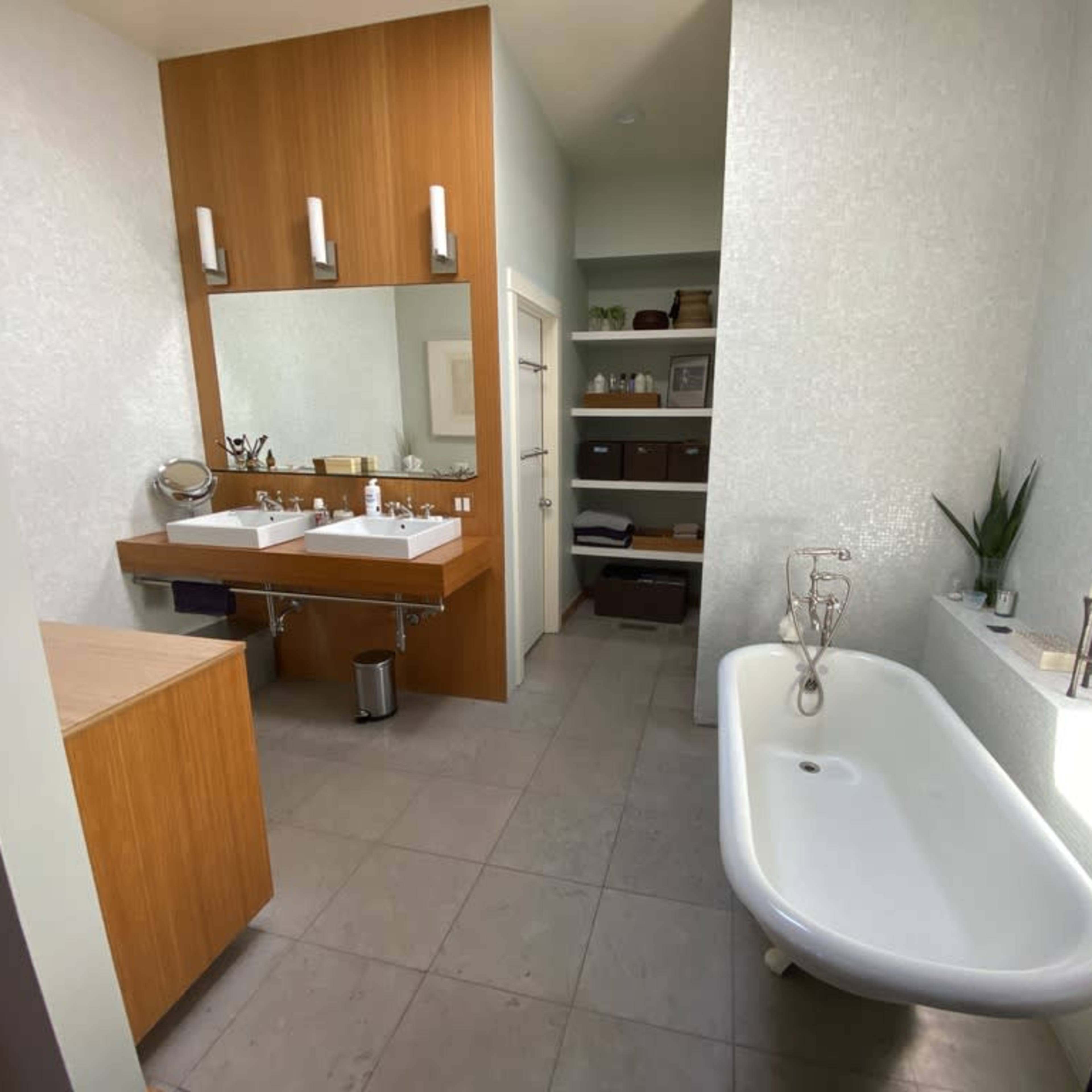 A modern bathroom featuring a freestanding bathtub, a double vanity with a large mirror, and shelves with neatly organized items.