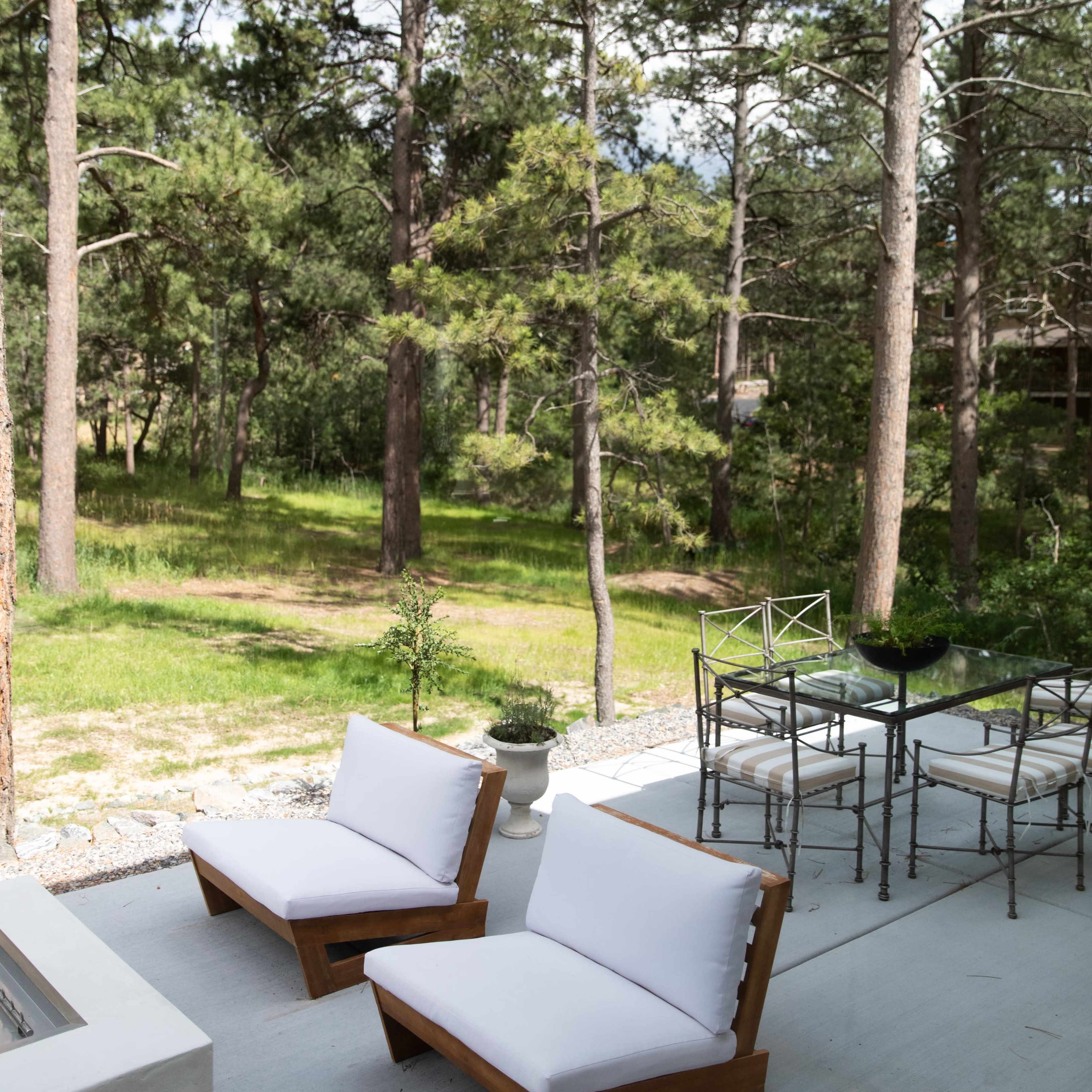 A patio area with two wooden lounge chairs and a dining table set against a backdrop of tall pine trees.