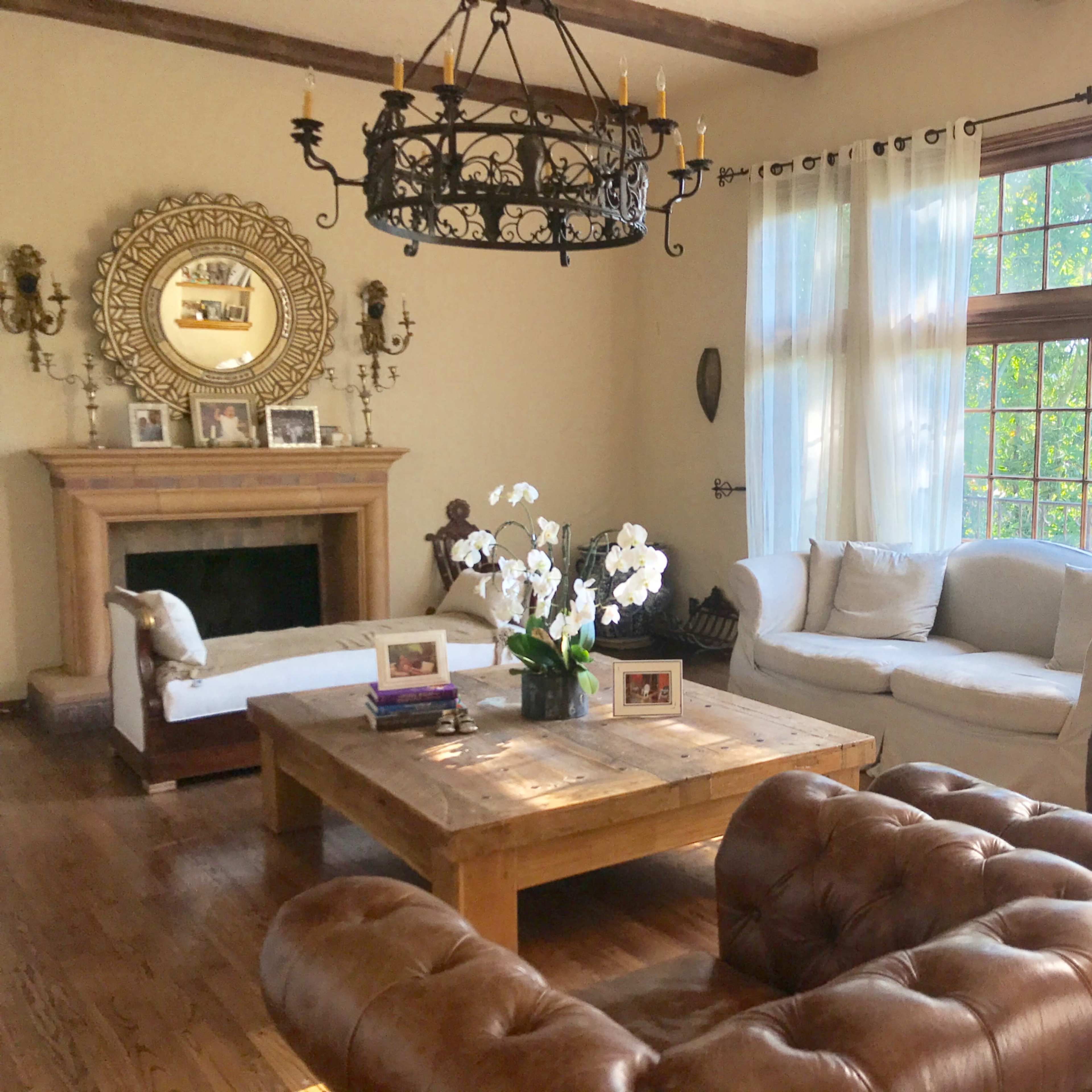 A cozy living room featuring a wooden coffee table, a white couch, a brown leather chair, and large windows with sheer curtains.