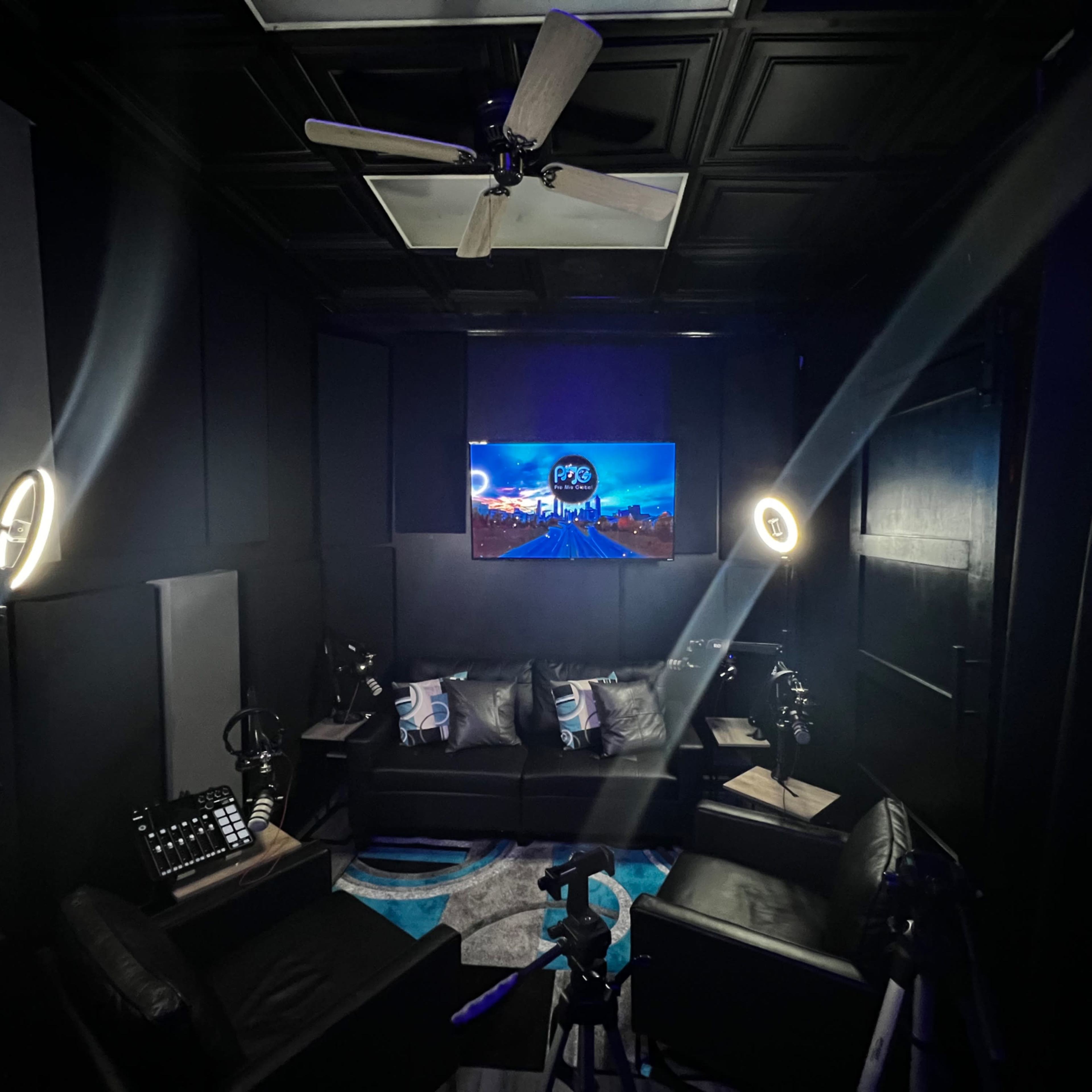 A dark studio with black walls, a large TV displaying a cityscape, and professional lighting setups surrounding a seating area.