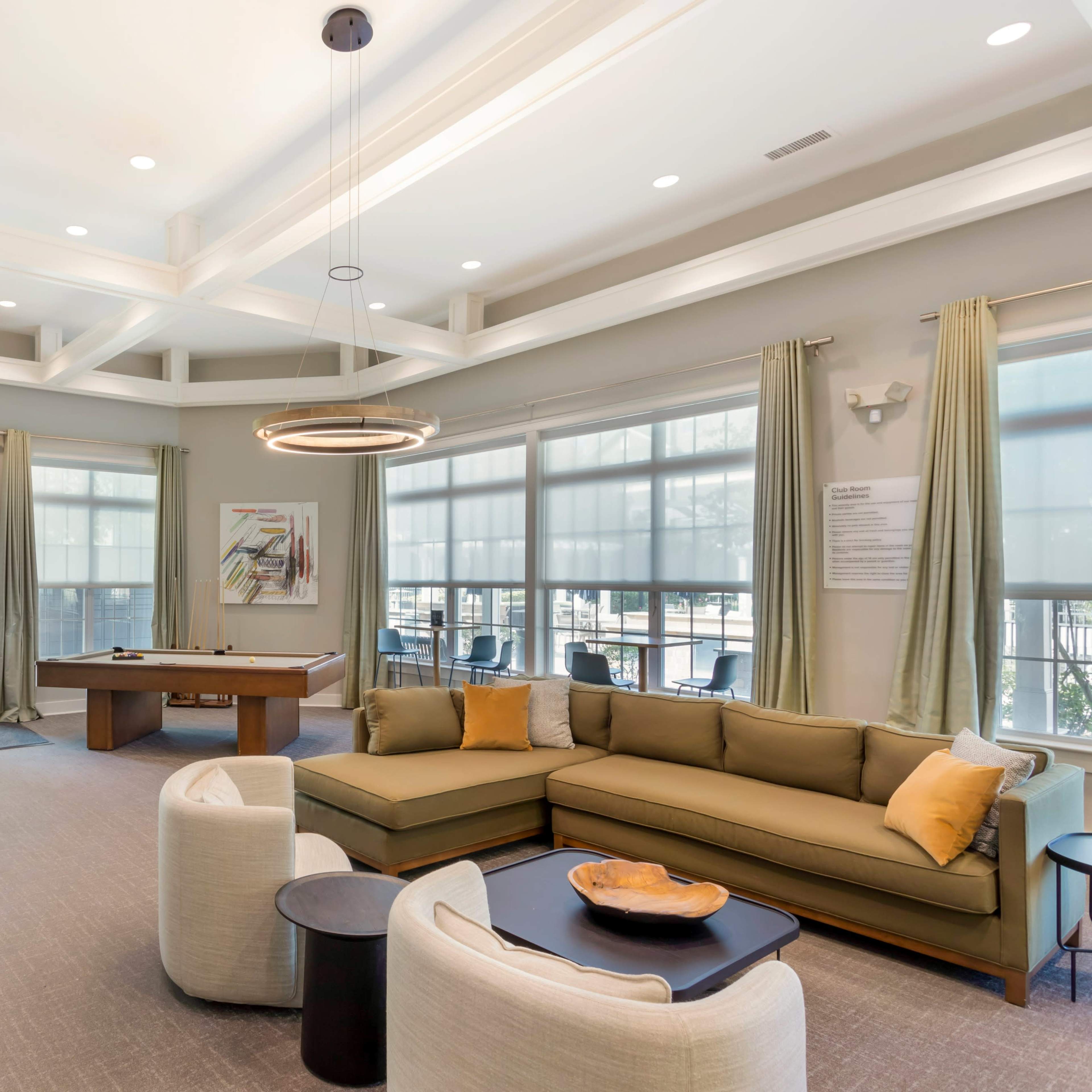 A well-lit lounge area with a large sectional sofa, a pool table, and art on the walls.