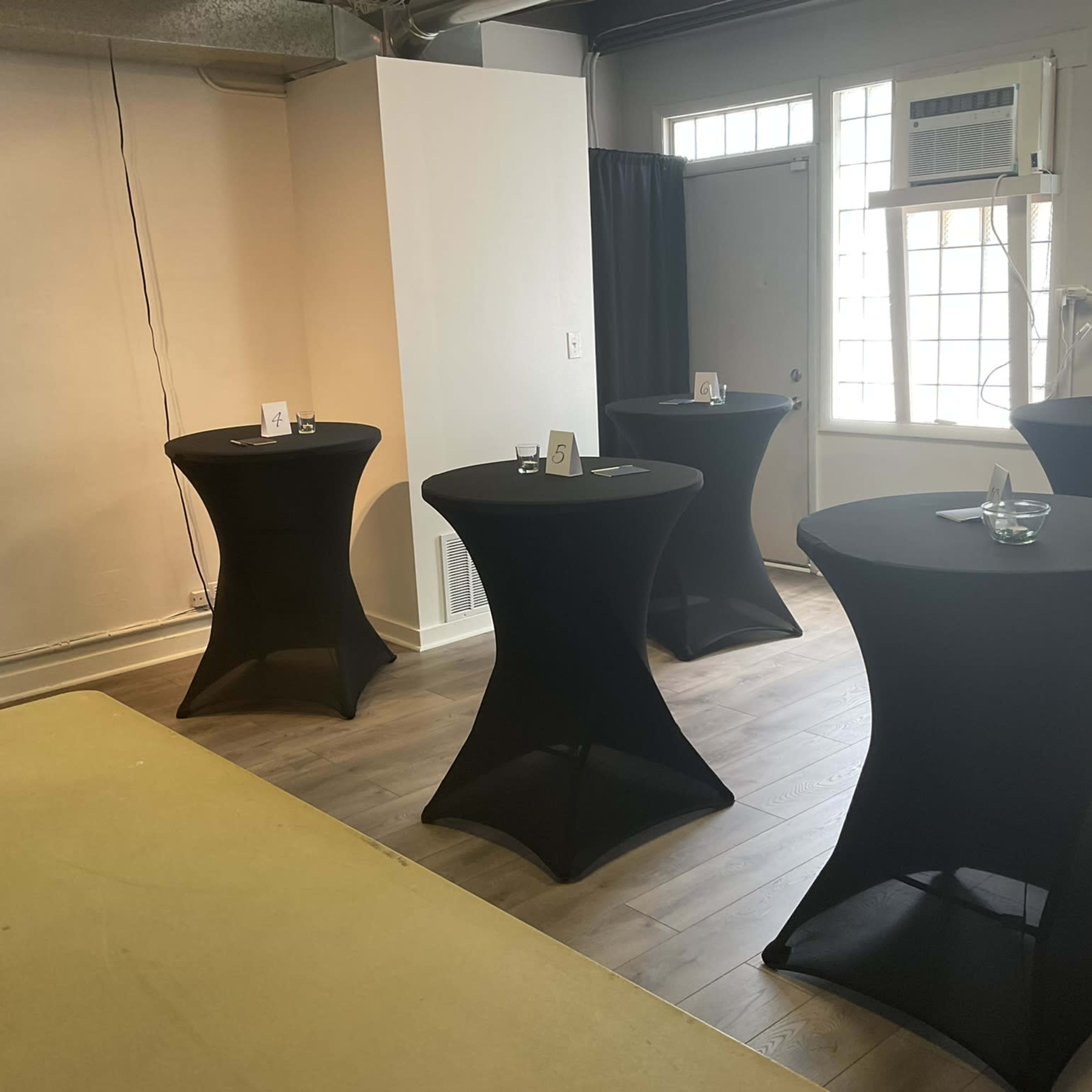 Several black cocktail tables arranged in a light-colored room with windows and a doorway.