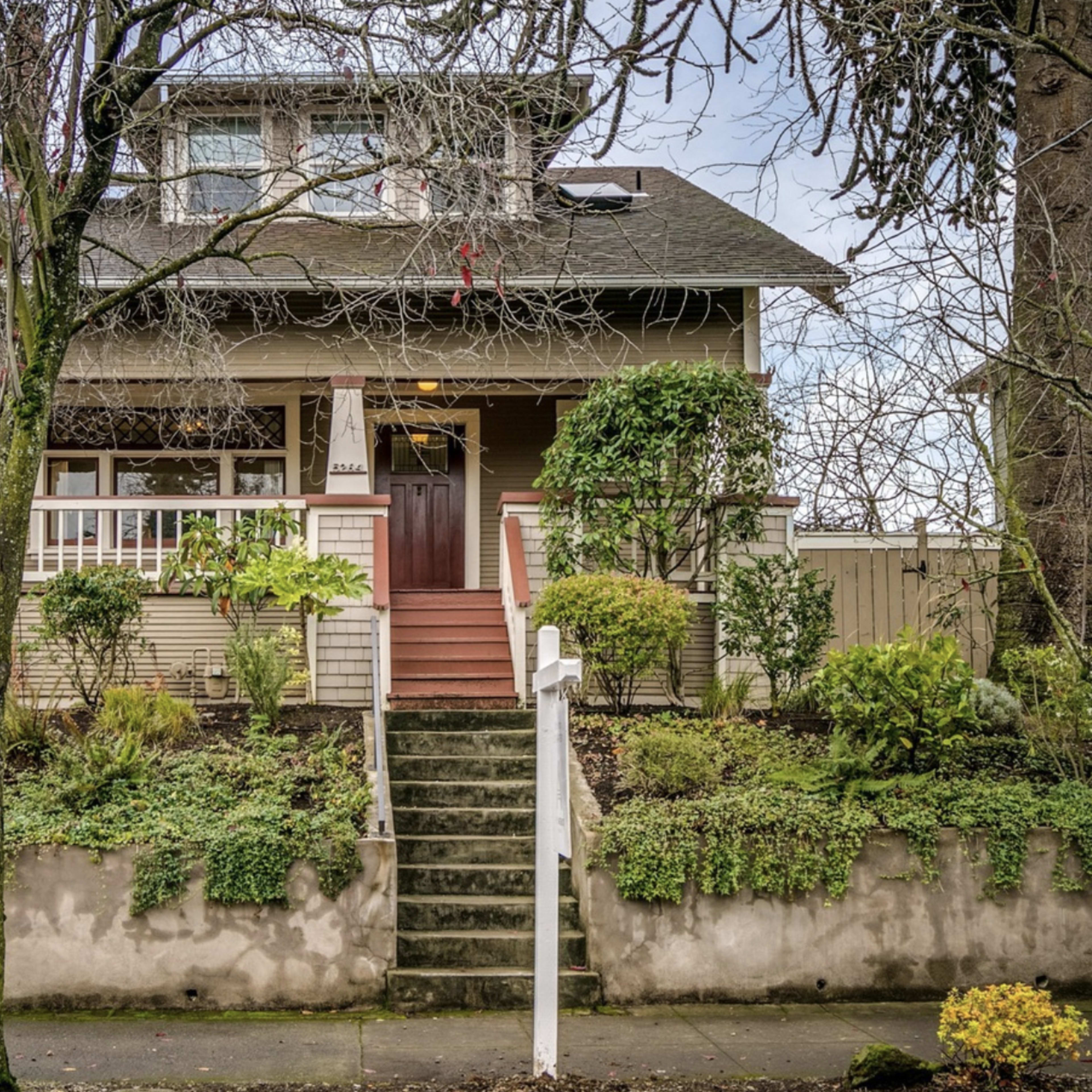 A two-story house with a front porch and landscaped garden is shown, featuring stairs leading up to the entrance.