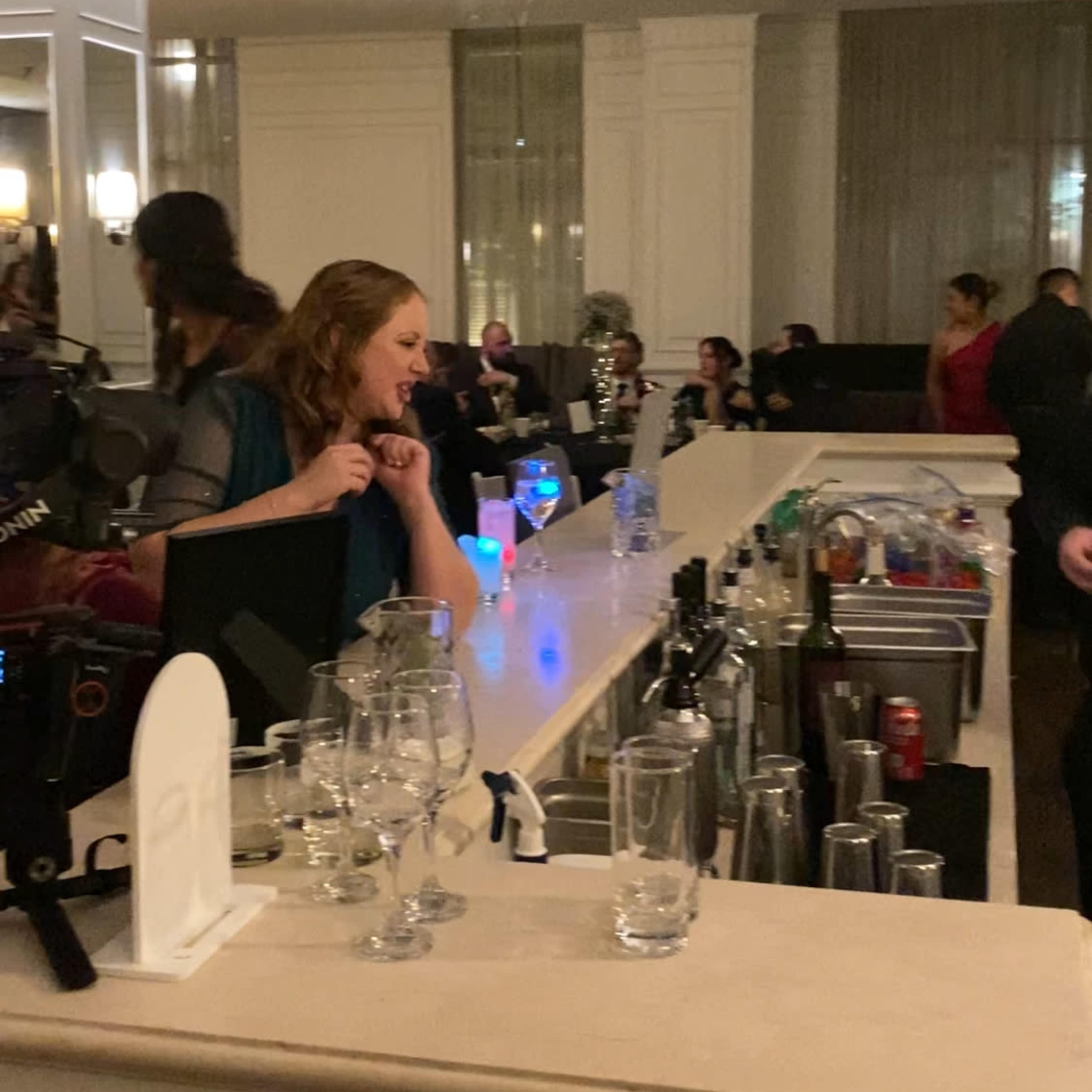 A bartender serves drinks at a well-lit bar while patrons socialize in the background.