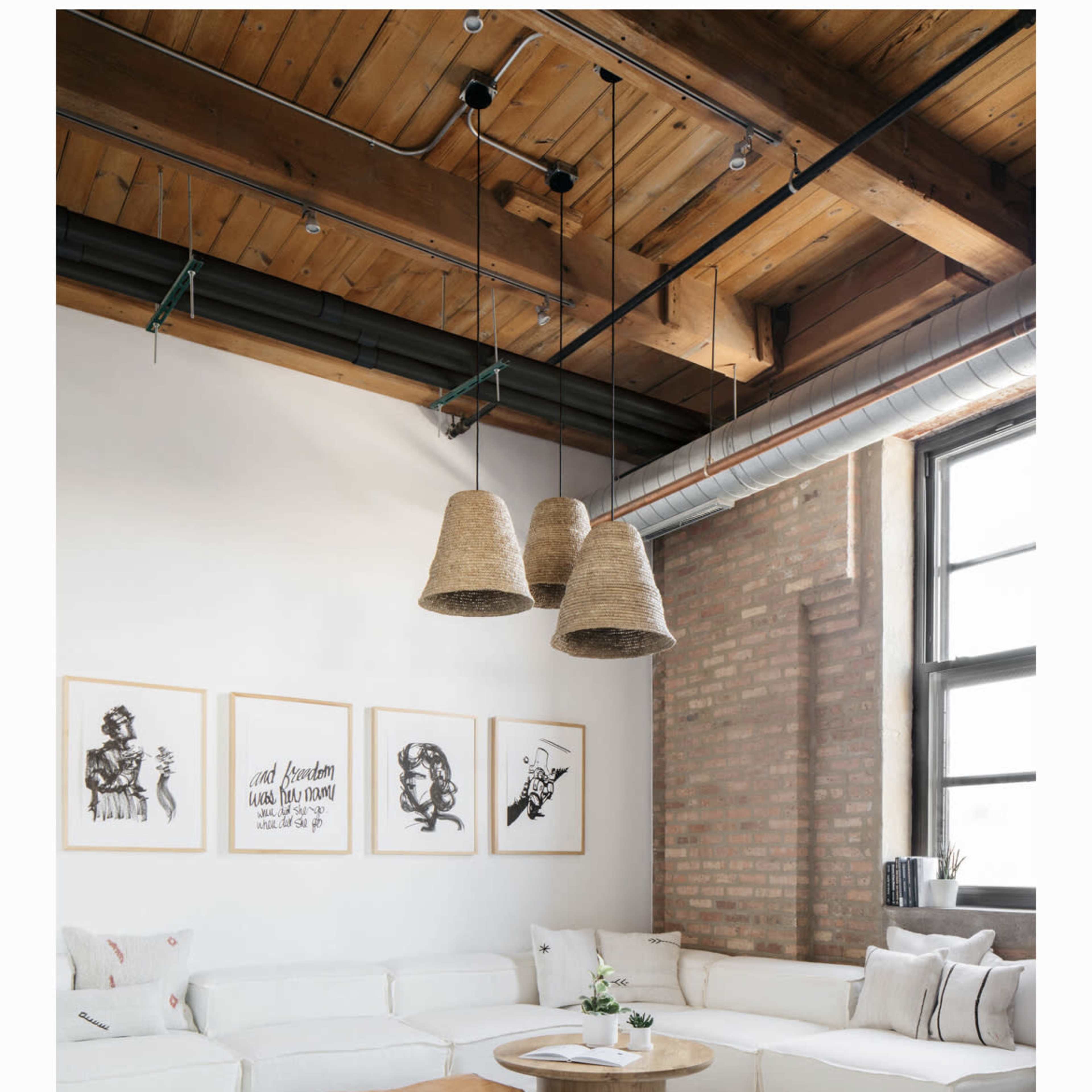 A modern living room features a white sectional sofa, a round coffee table, and three large pendant lights hanging from the ceiling, with artwork displayed on the walls and a plush rug on the floor.