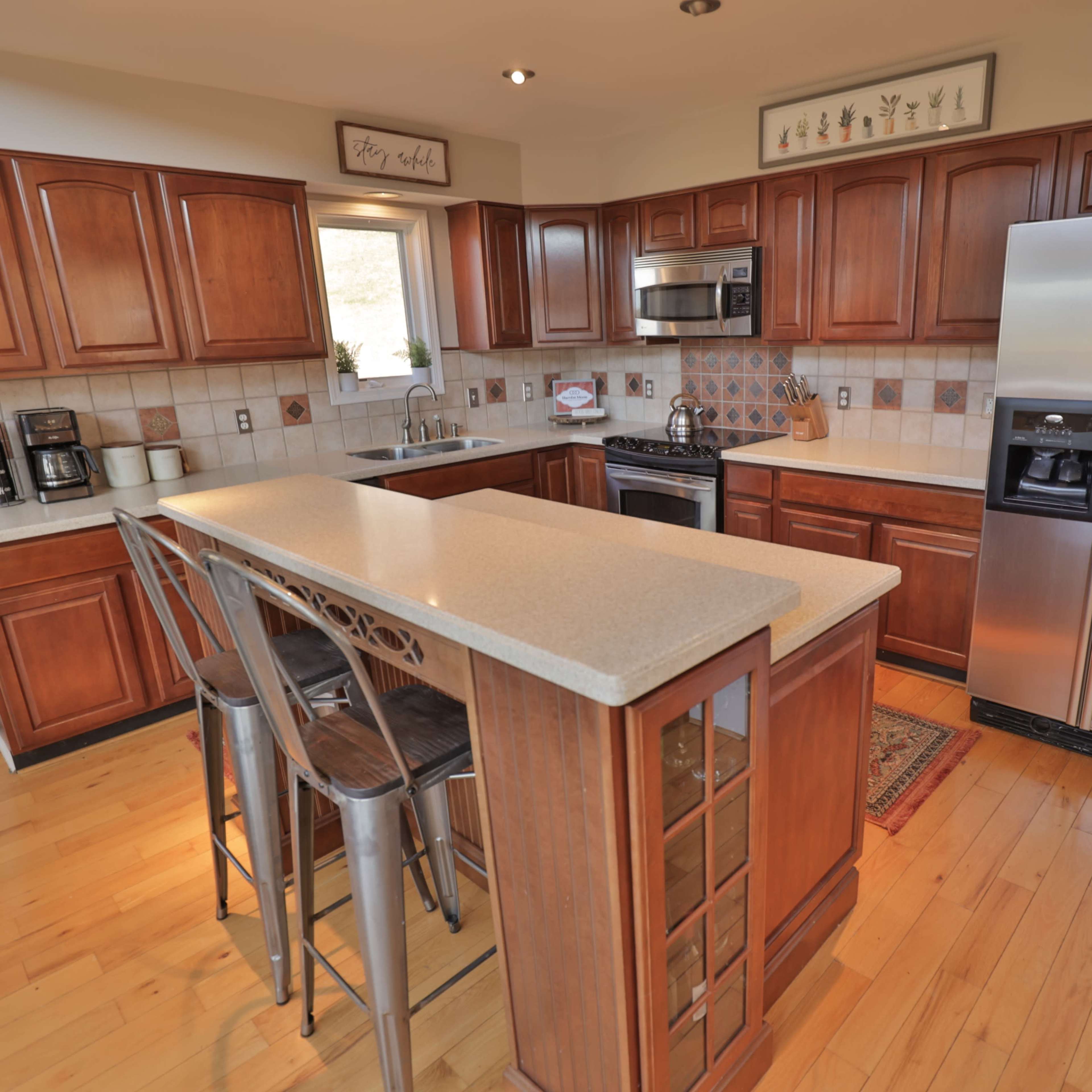 The kitchen features wooden cabinetry, a central island with seating, and stainless steel appliances.