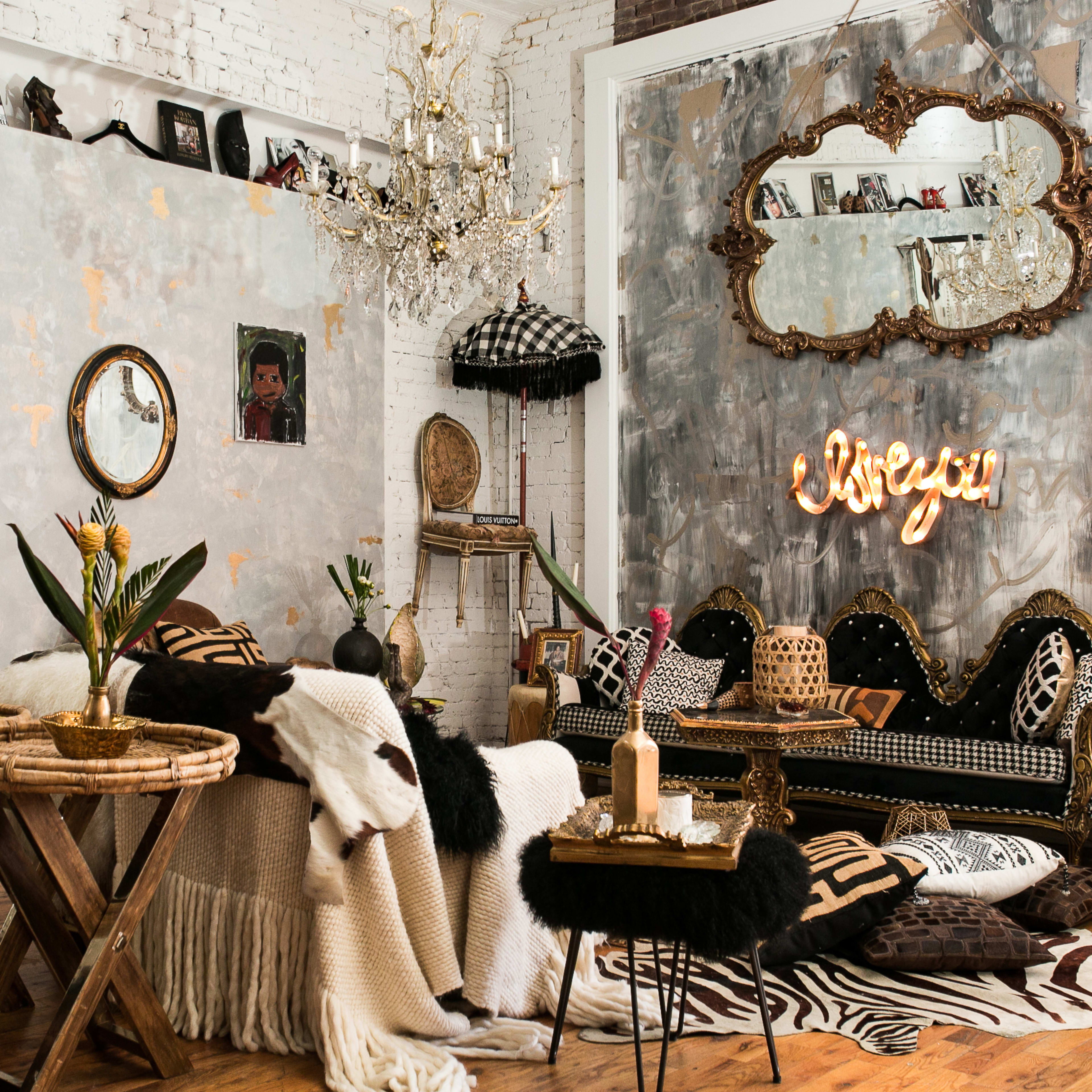 A stylish living room with a mix of vintage and modern decor, featuring a black and gold sofa, a chandelier, and textured wall art.