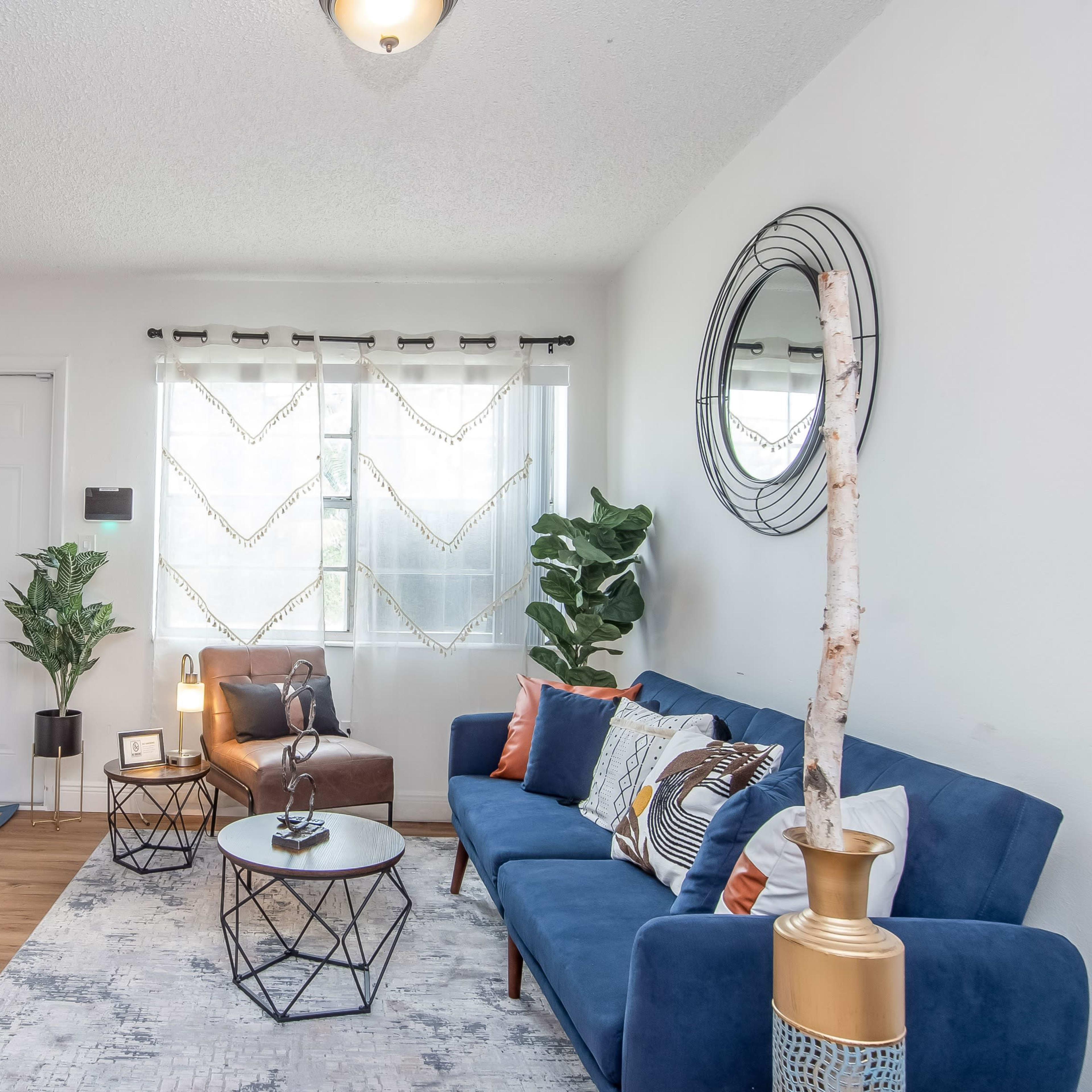 A modern living room with a blue sofa, two side tables, a large mirror, and natural light coming through windows.