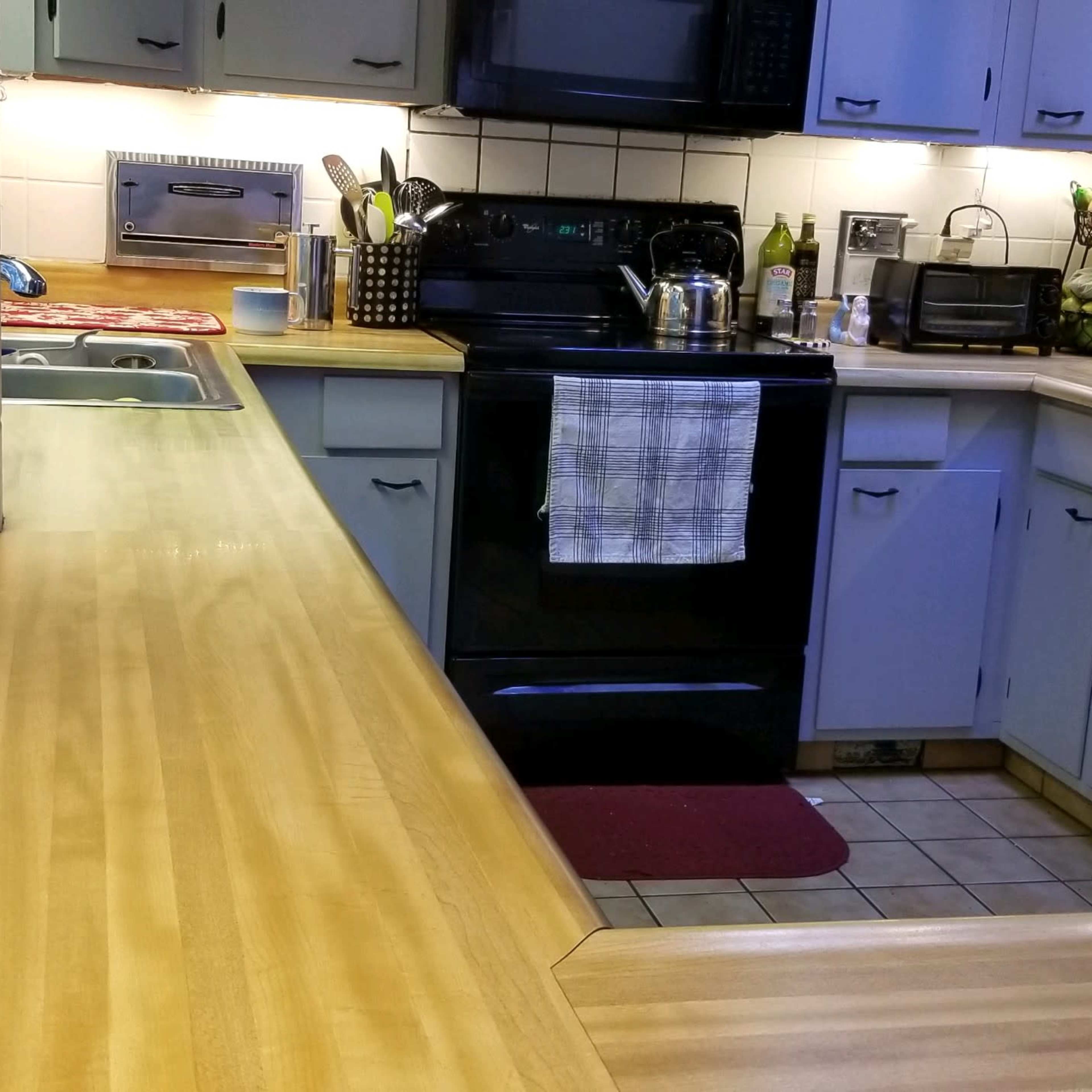A well-lit kitchen features a wooden countertop, black appliances, and various utensils arranged on the counter.
