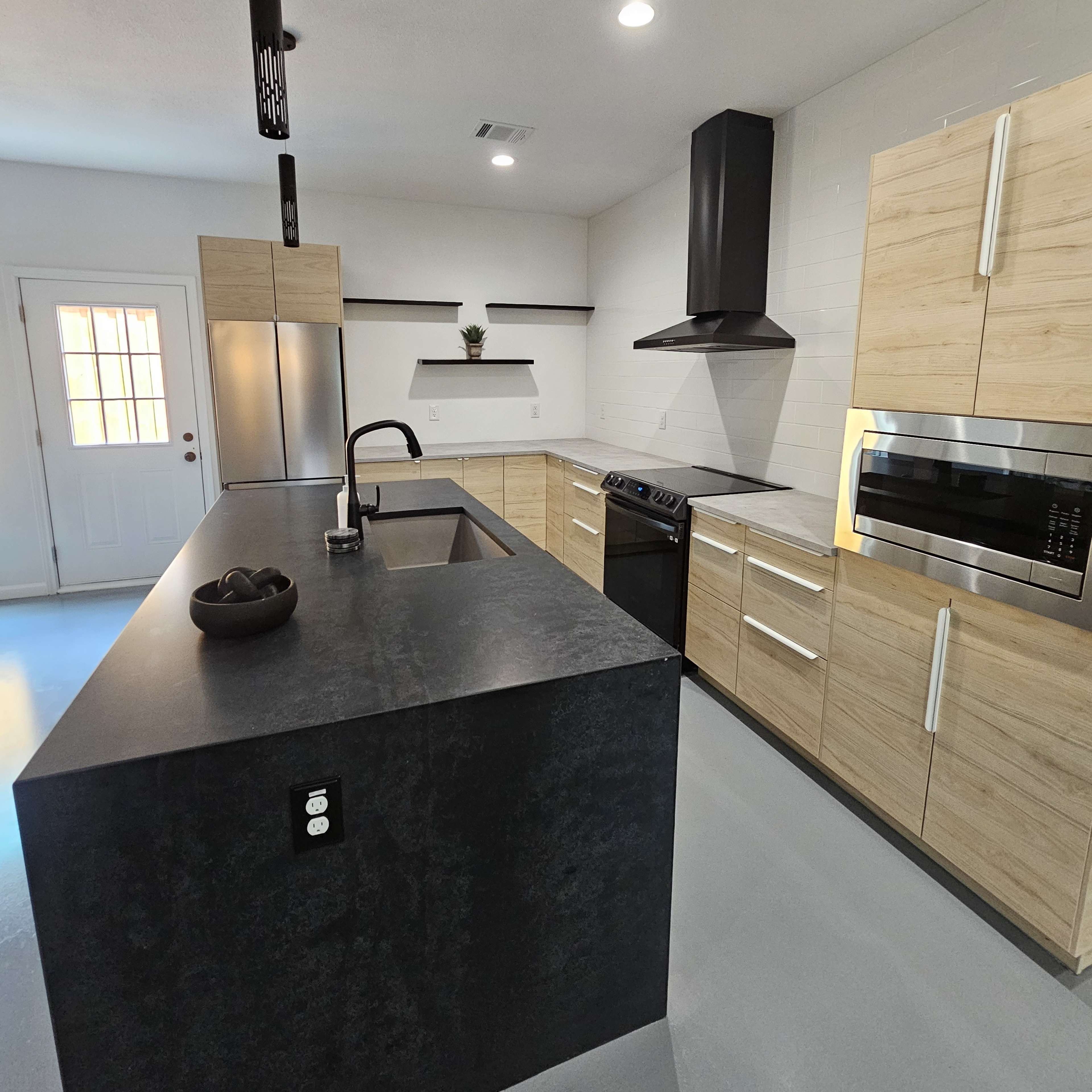 A modern kitchen with a central island, stainless steel appliances, and wooden cabinetry, illuminated by overhead lighting.