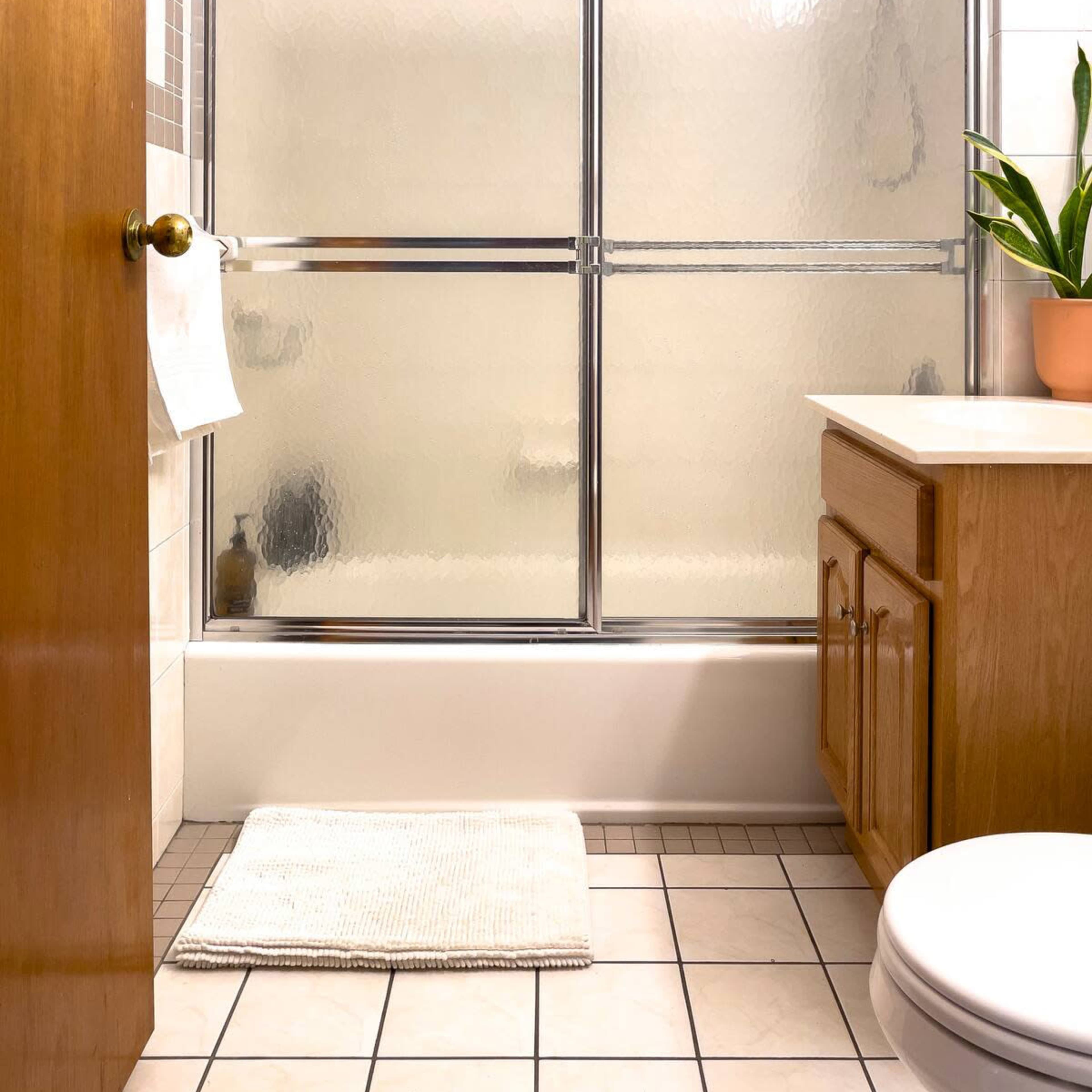 A bathroom with a shower enclosed by glass doors, a wooden cabinet, a toilet, and a potted plant on the countertop.