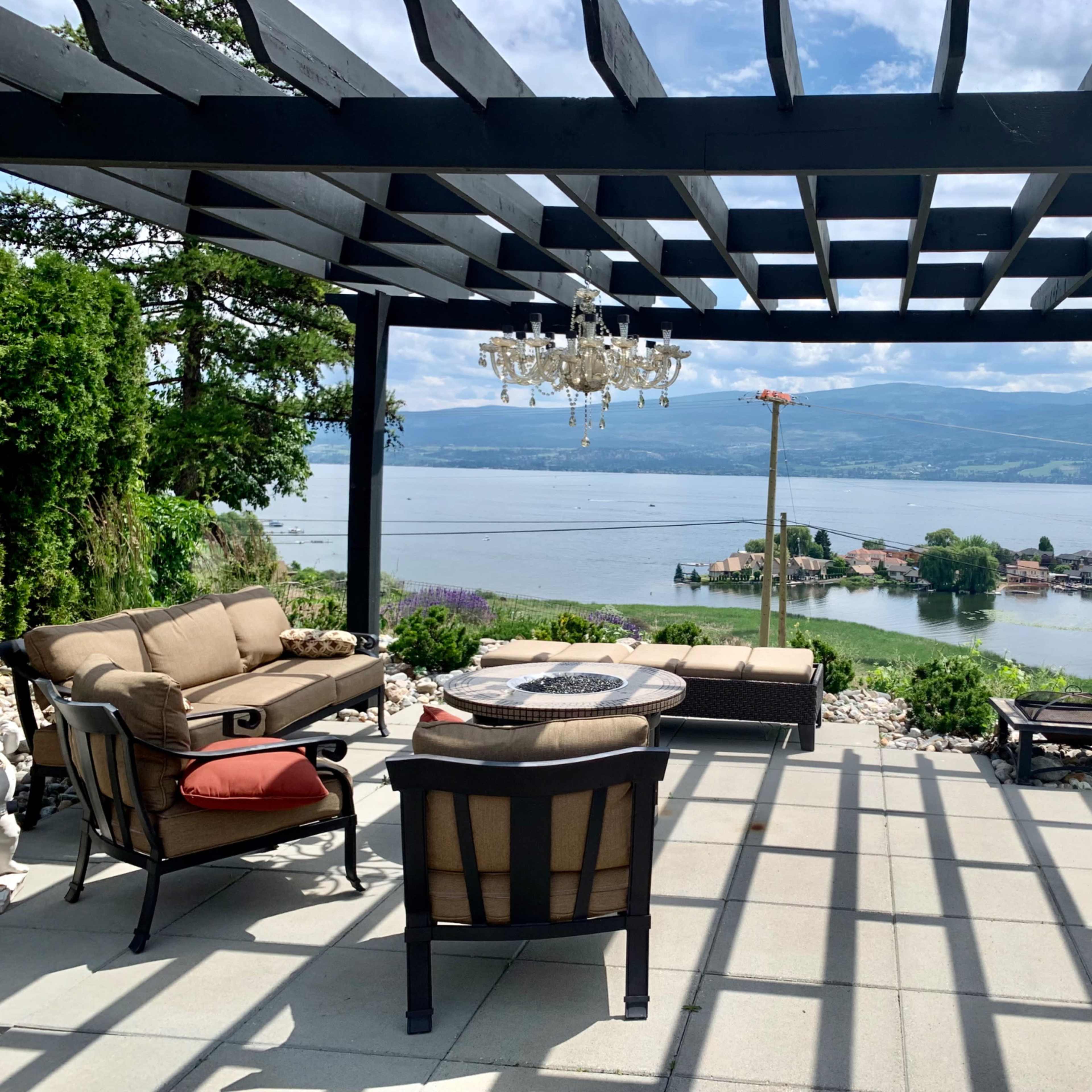 A patio with a pergola features outdoor seating and a view of a lake and distant hills.