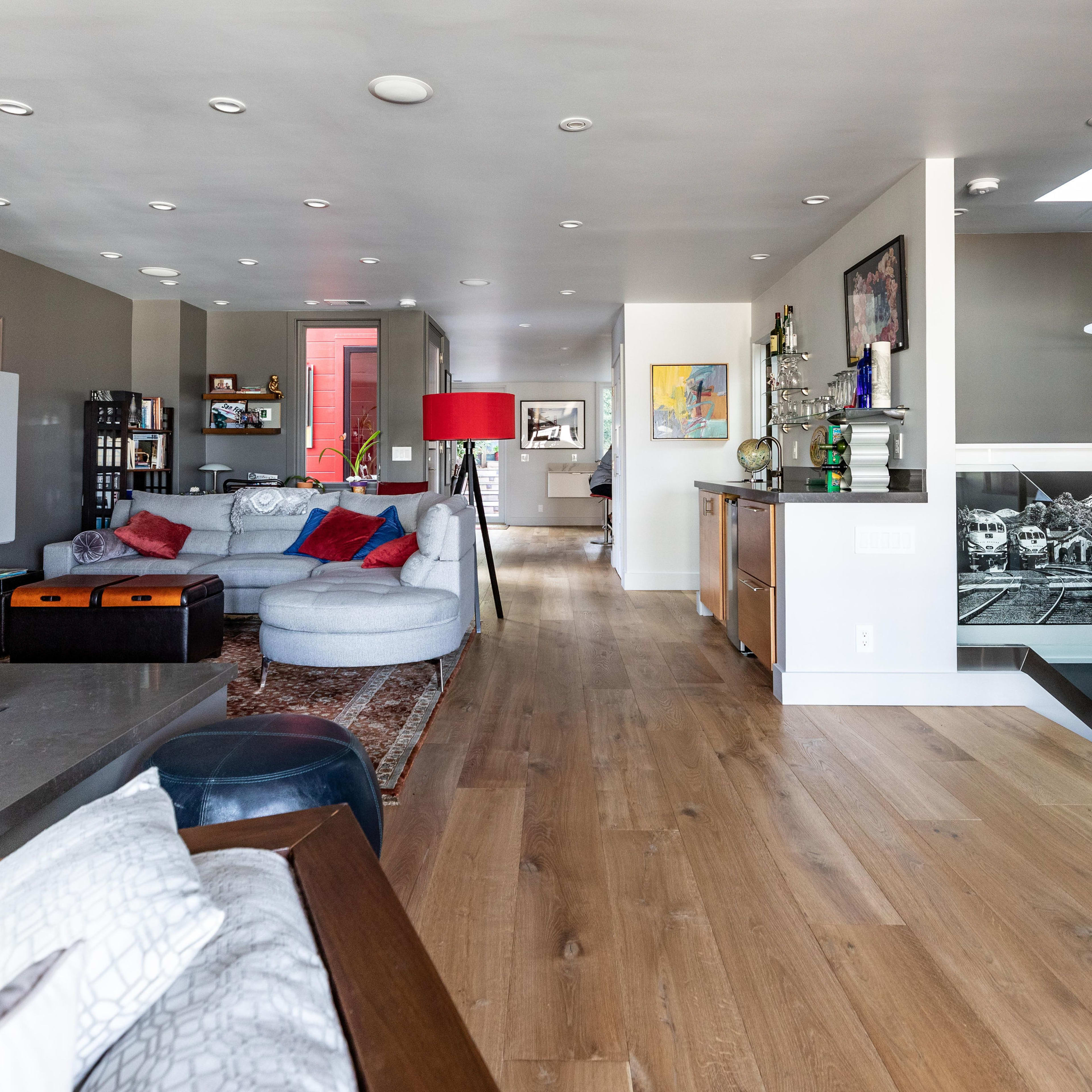 A modern interior space featuring an open living area with a blue sectional couch, a dining area, a kitchenette, and a staircase leading to a lower level.