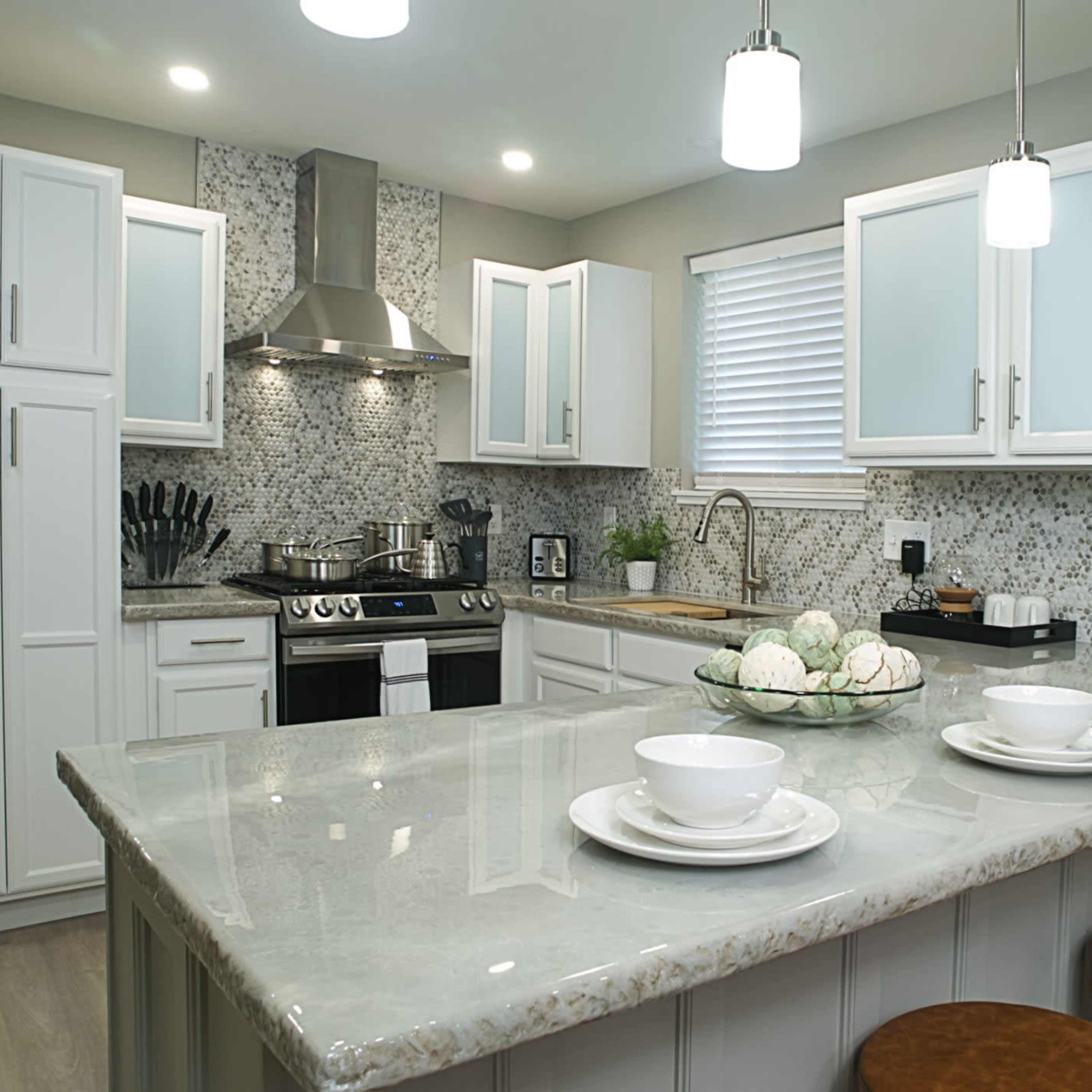 A modern kitchen with white cabinets, a gray countertop, and pendant lighting above a central island.