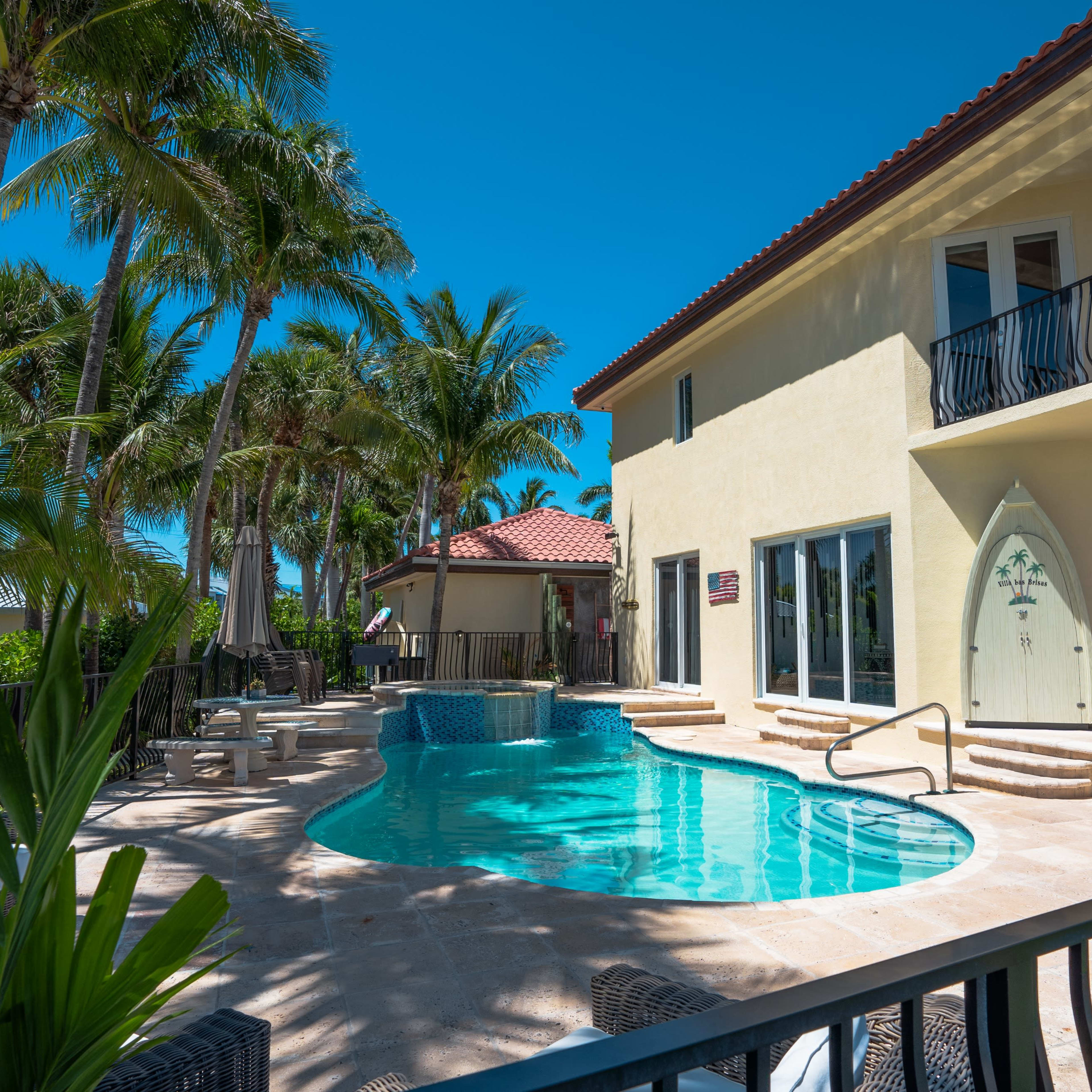 A luxurious home features a swimming pool surrounded by palm trees and outdoor seating areas.