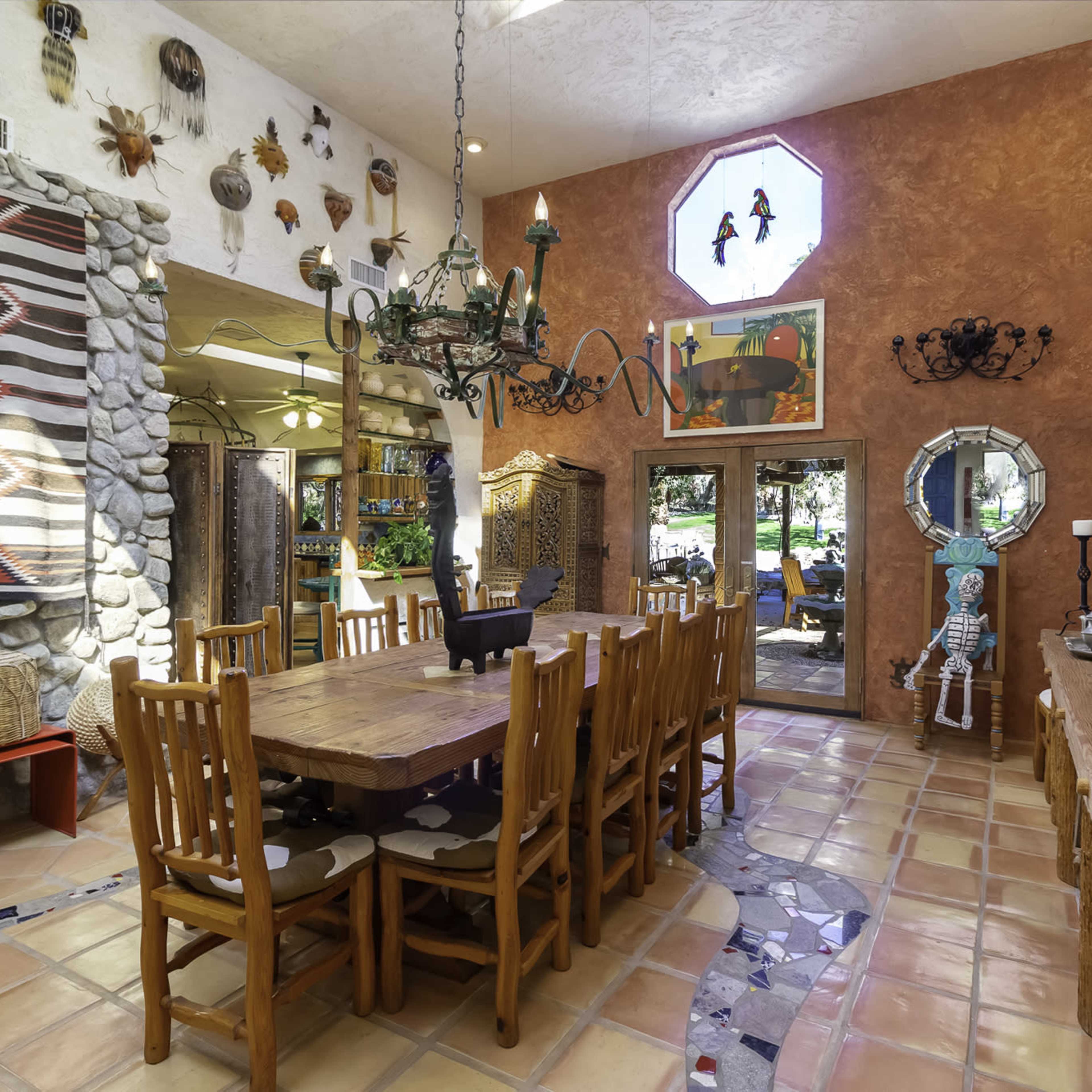 A spacious dining area featuring a large wooden table surrounded by chairs, with decorative wall hangings and a stone wall.