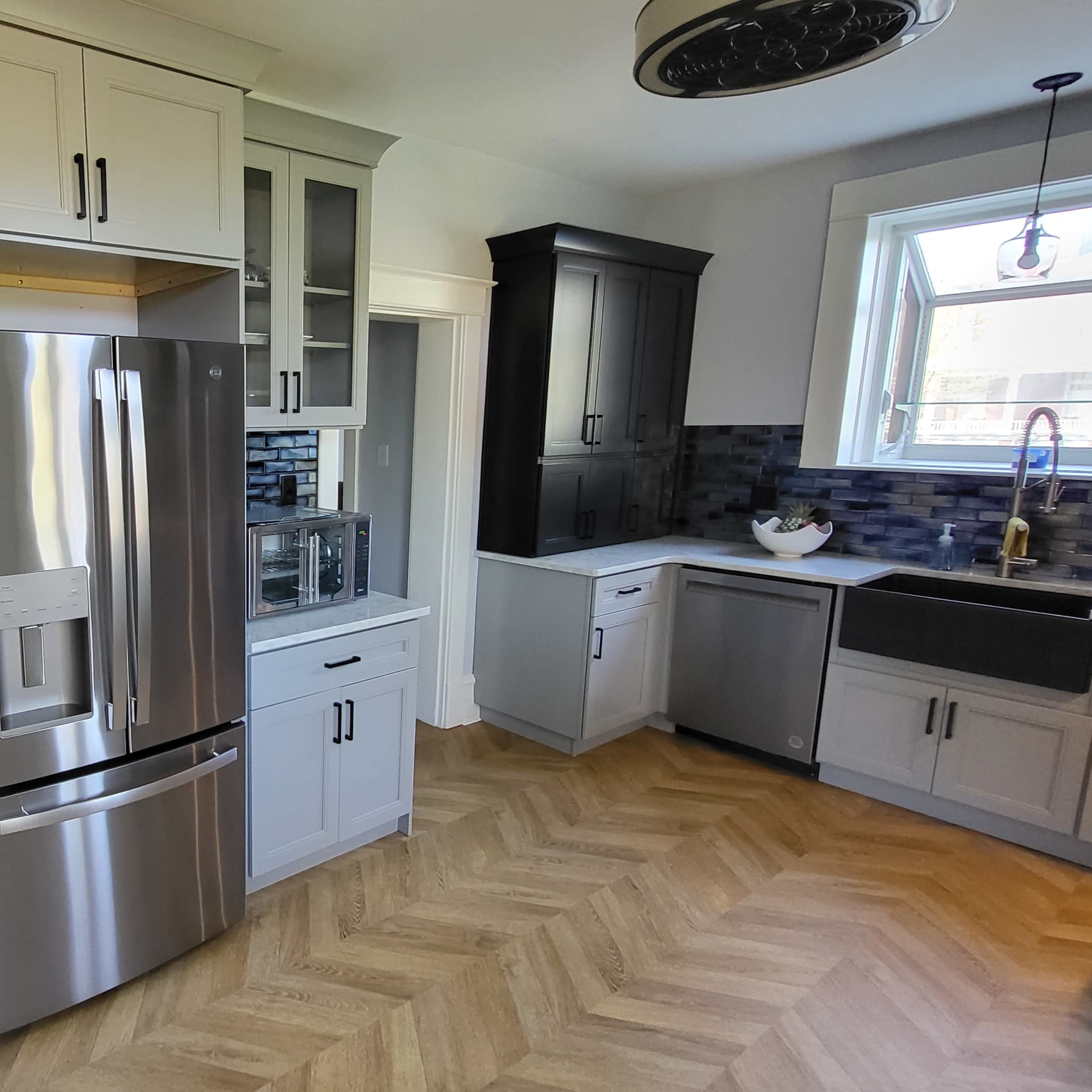 A modern kitchen featuring a stainless steel refrigerator, a farmhouse sink, and a staircase leading to an upper level.