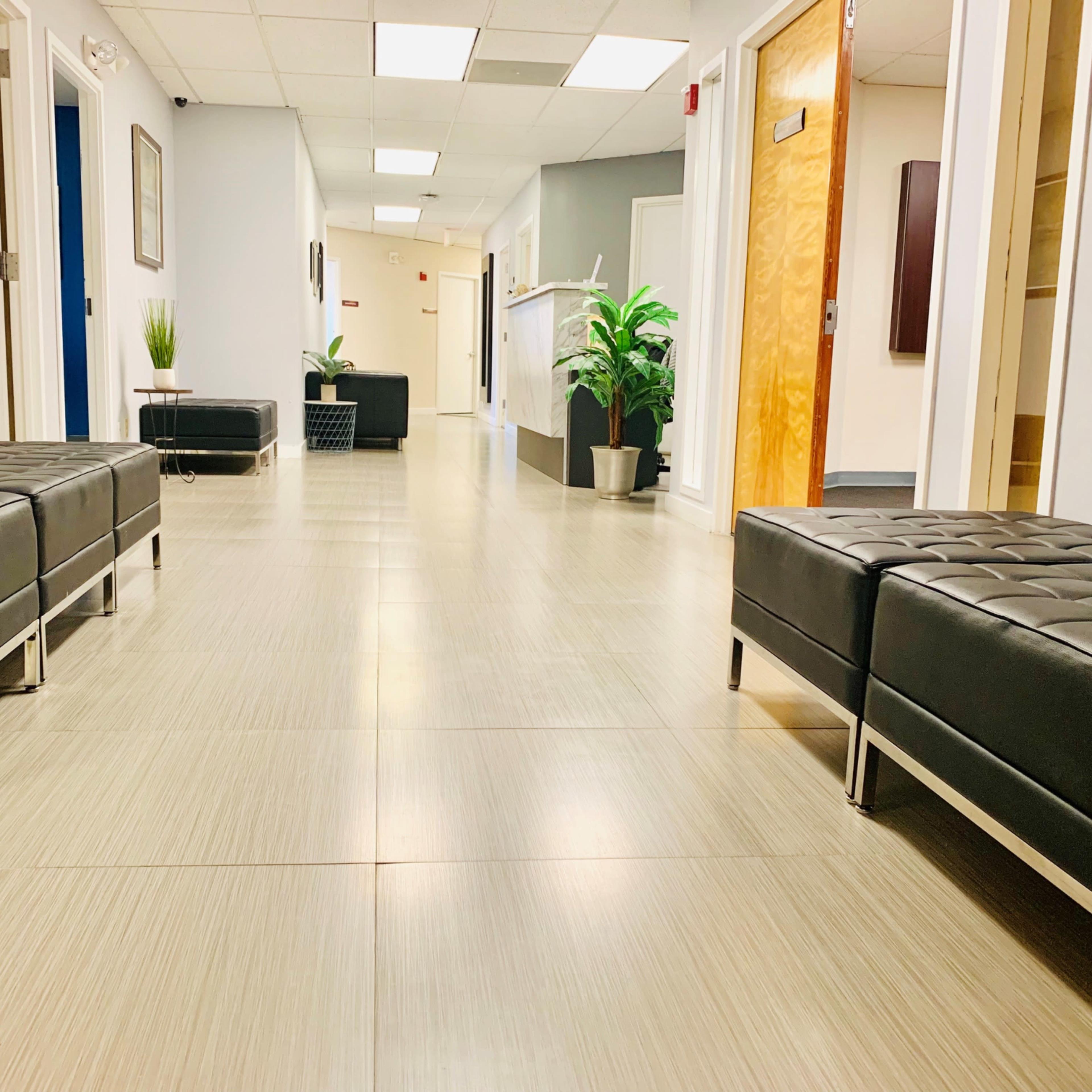 A modern hallway with two black benches on either side, leading to a reception area at the end.