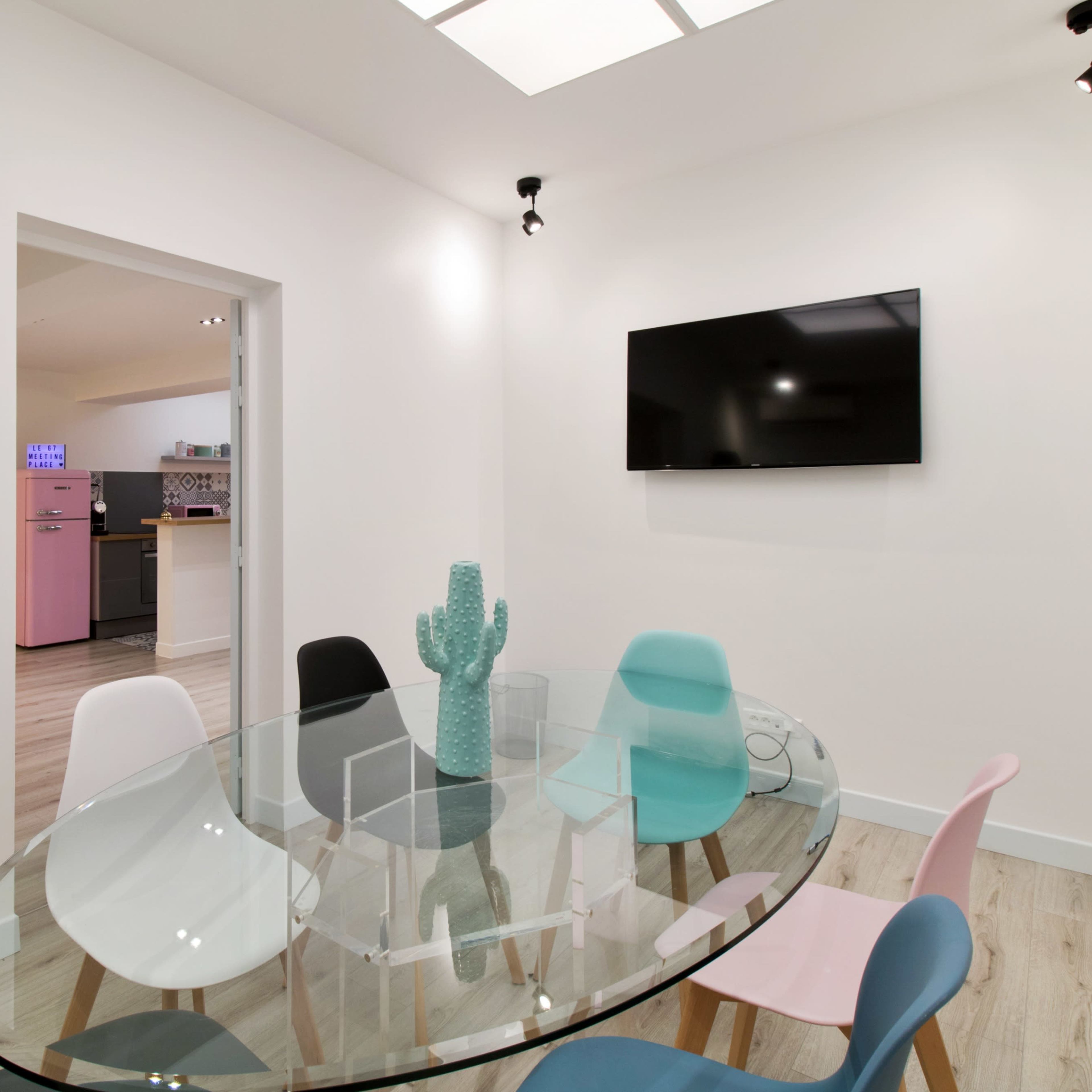 A modern dining area features a round glass table surrounded by colorful chairs and a wall-mounted television.
