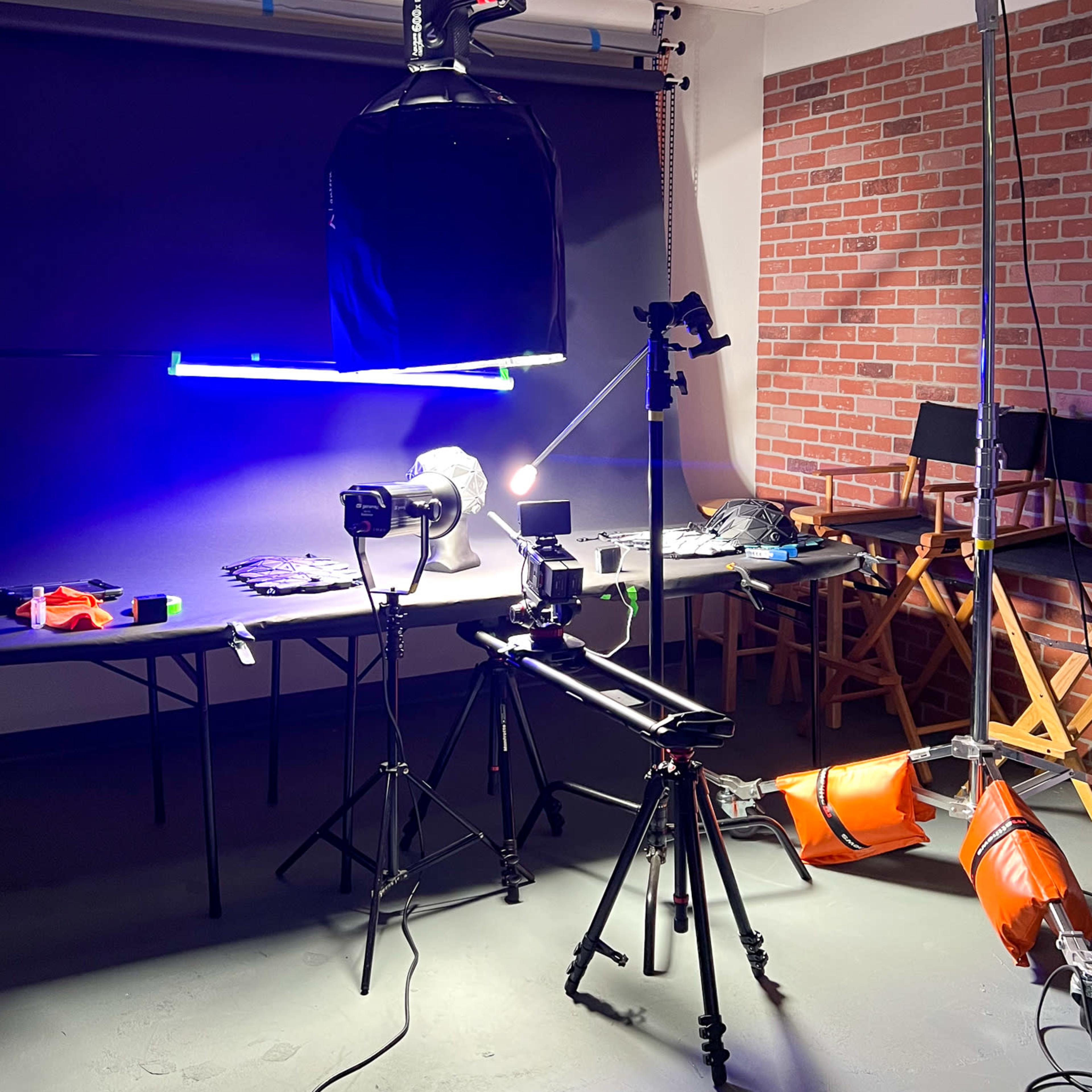 A photography studio setup with various camera equipment, lighting, and props arranged on tables against a brick wall.