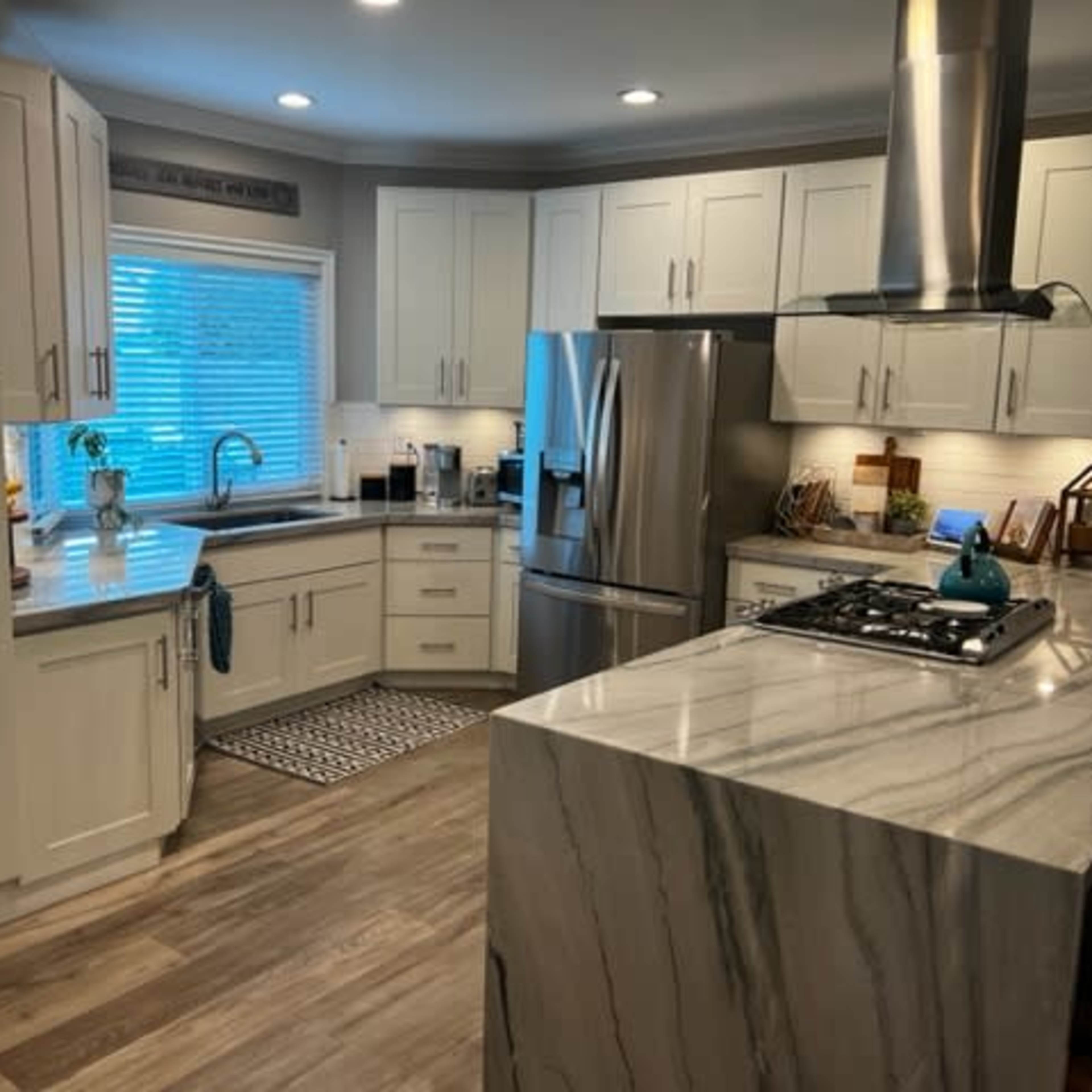 A modern kitchen features white cabinetry, stainless steel appliances, and a marble-topped island with a gas stove.