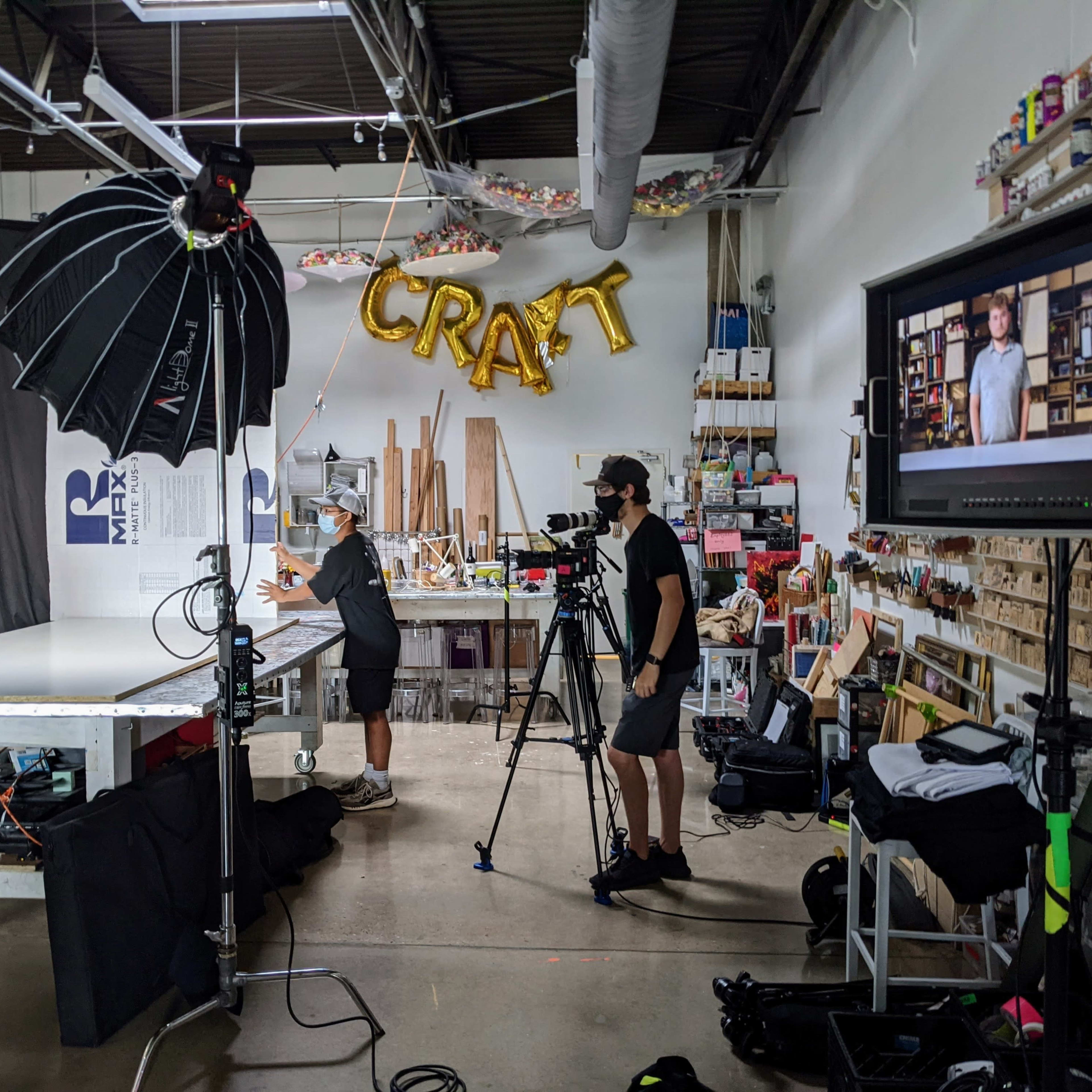 A photography studio is set up with a large backdrop and bright lights, featuring two people interacting while a camera records the scene.