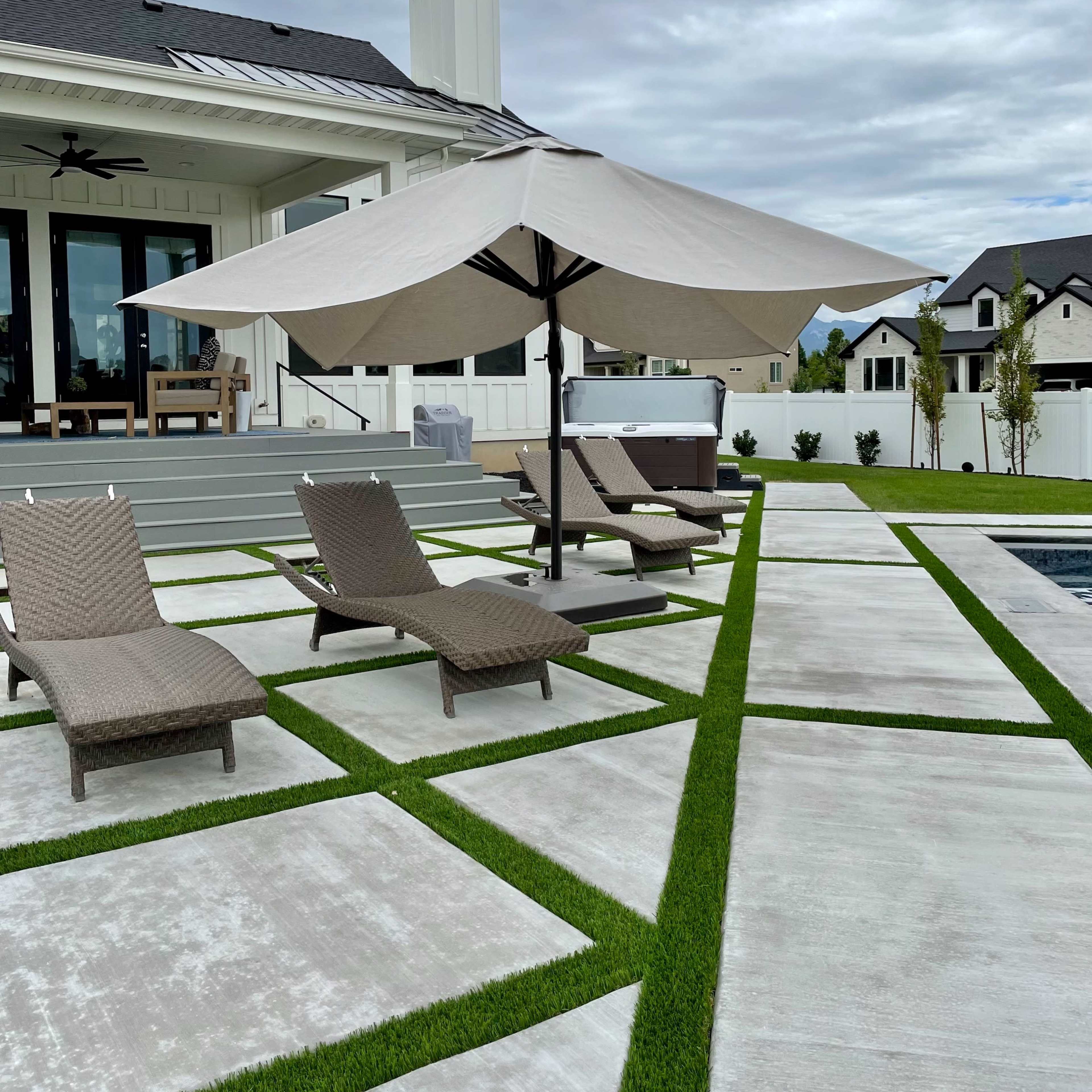 A large patio area features loungers with a shaded umbrella and a pool against a backdrop of a modern house.
