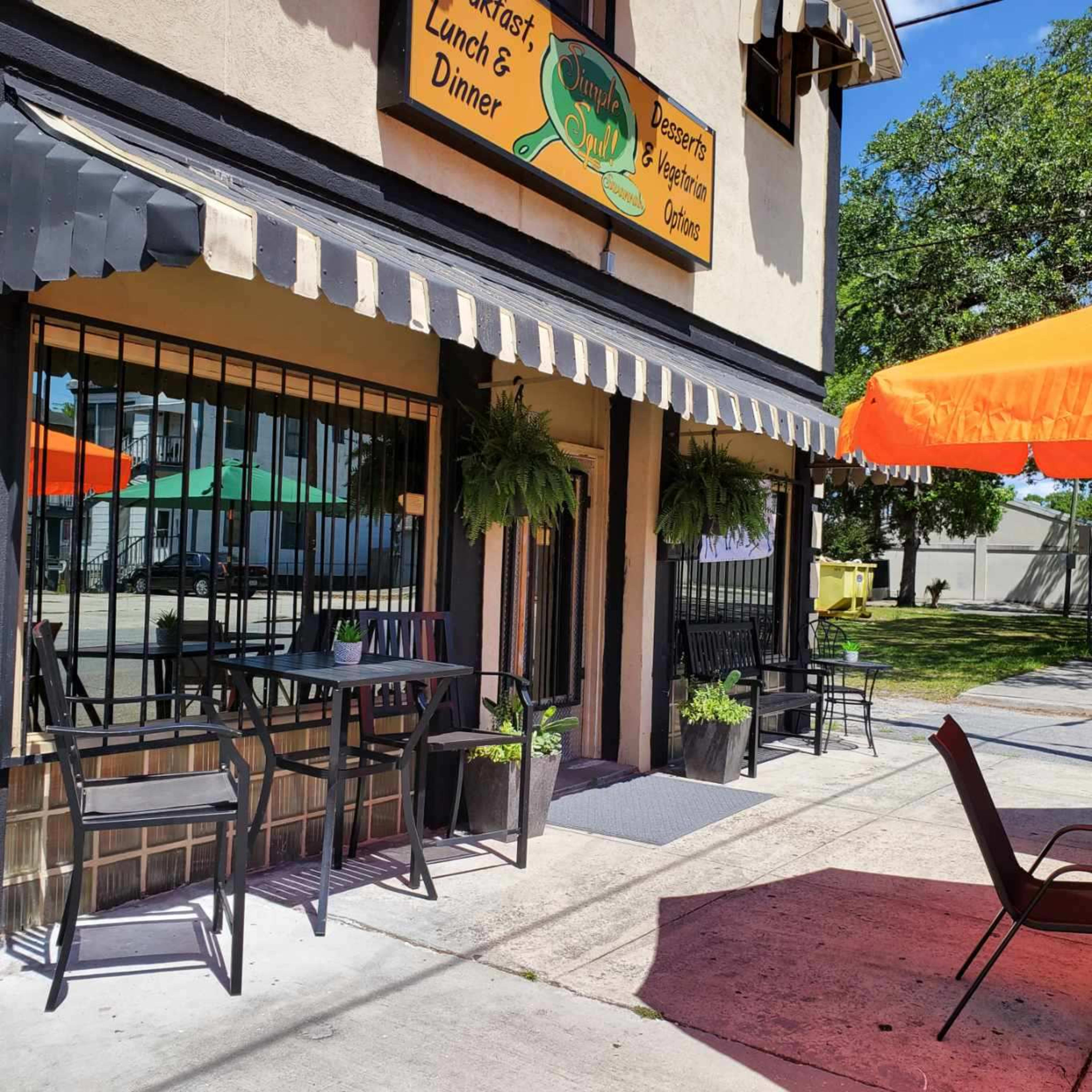 A restaurant with black chairs and tables sits under an awning, featuring a sign that reads "Linda's Lunch & Dinner" and orange umbrellas at outdoor seating.