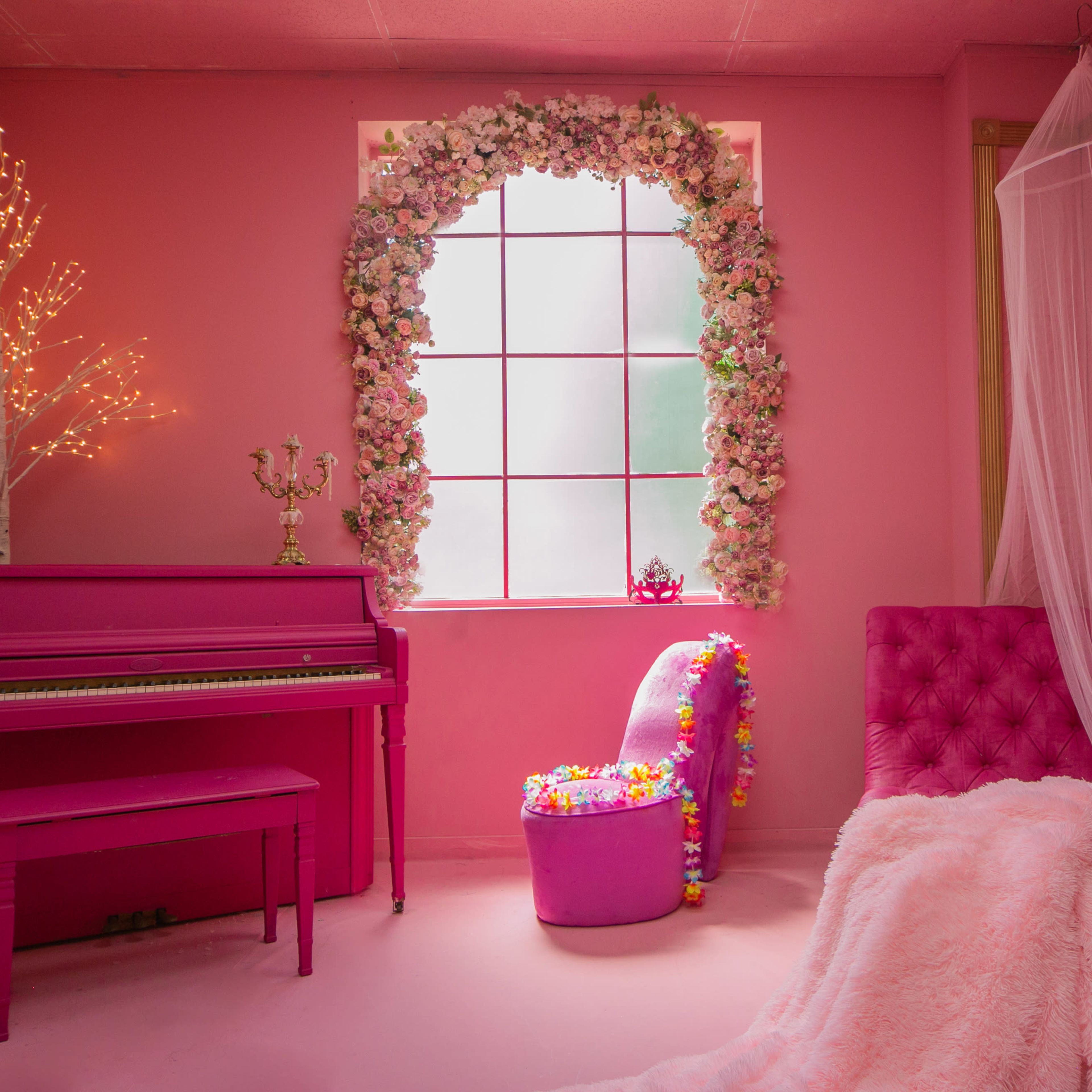 A pink-themed room featuring a pink piano, a chair adorned with flowers, and a window framed with floral decorations.