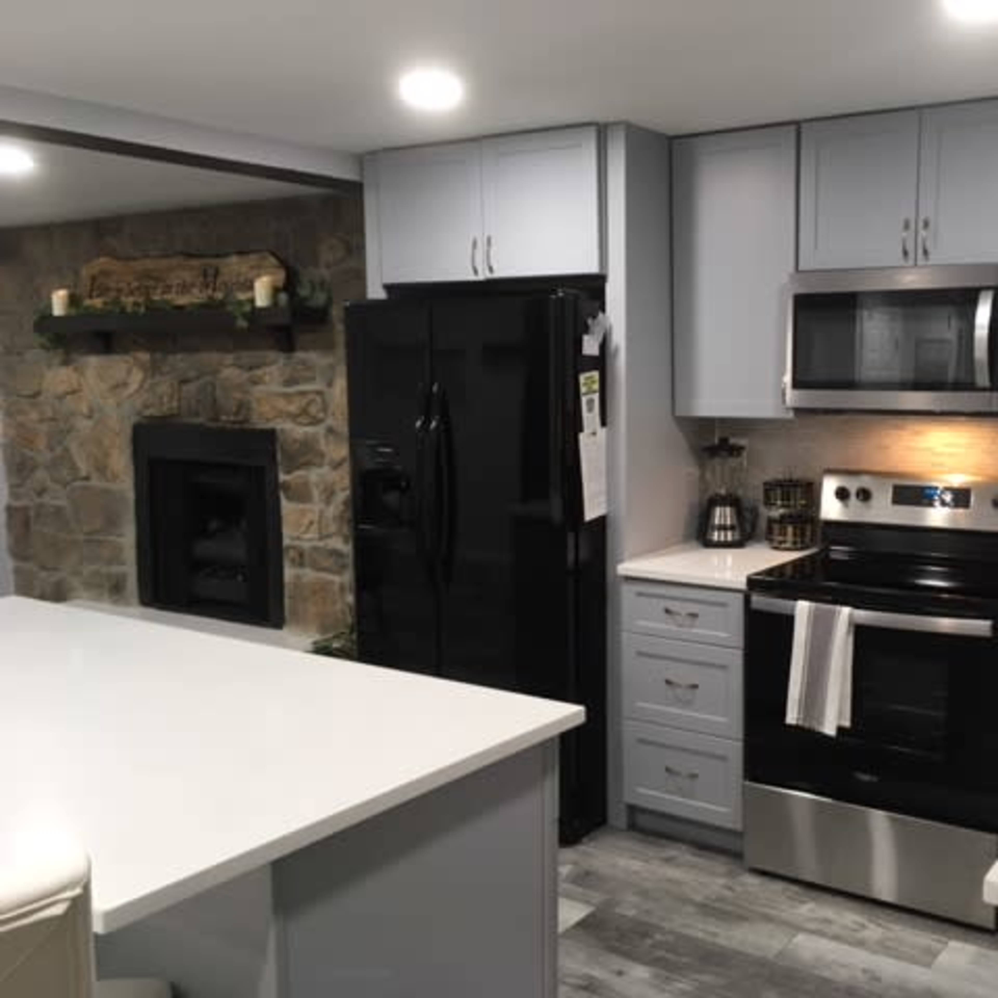 A modern kitchen featuring gray cabinetry, a black refrigerator, and a stainless steel oven and microwave.