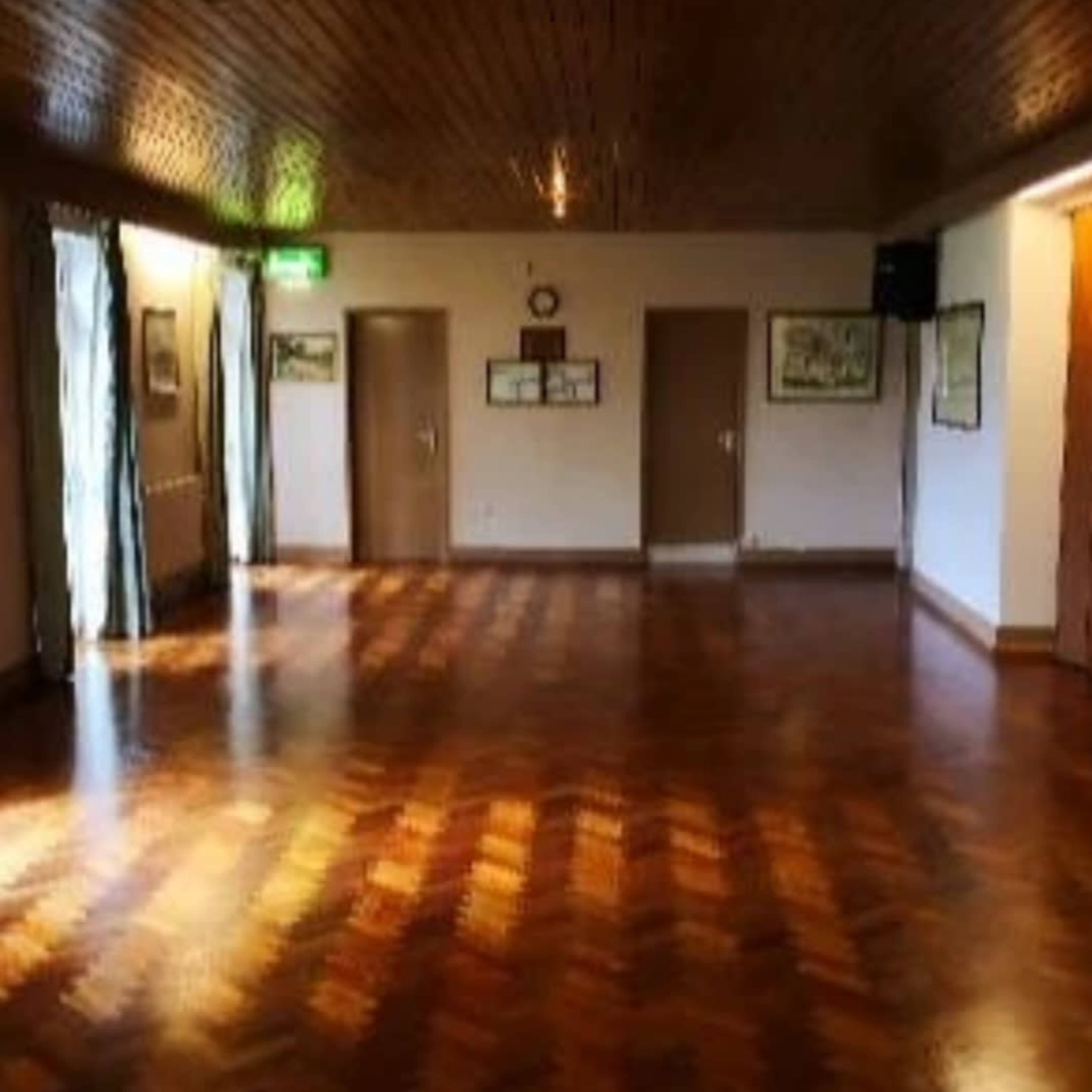 An empty room with polished wooden flooring, walls adorned with framed artworks, and three doors leading to other areas.