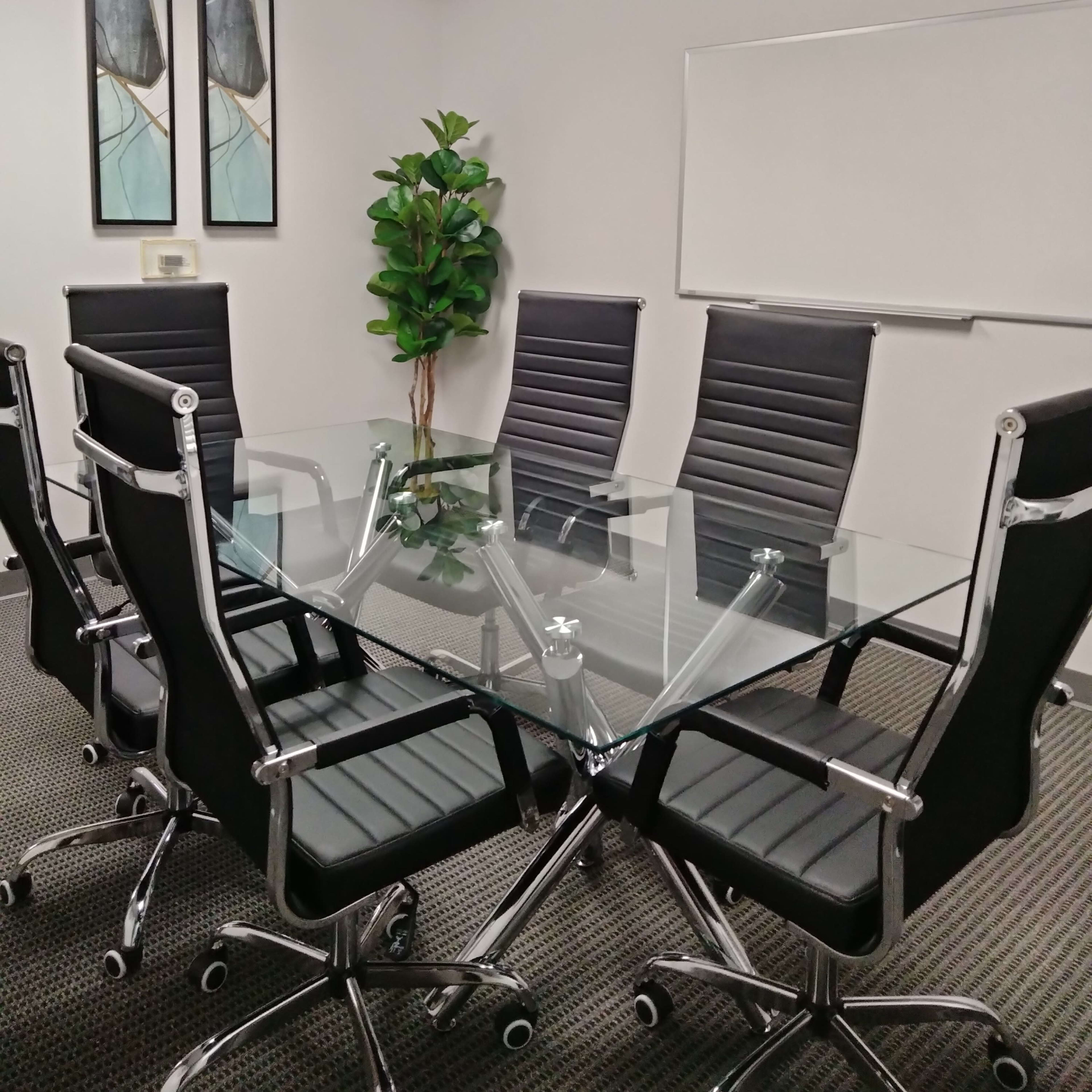 A modern conference room with a glass table surrounded by six black leather chairs and a whiteboard on the wall.