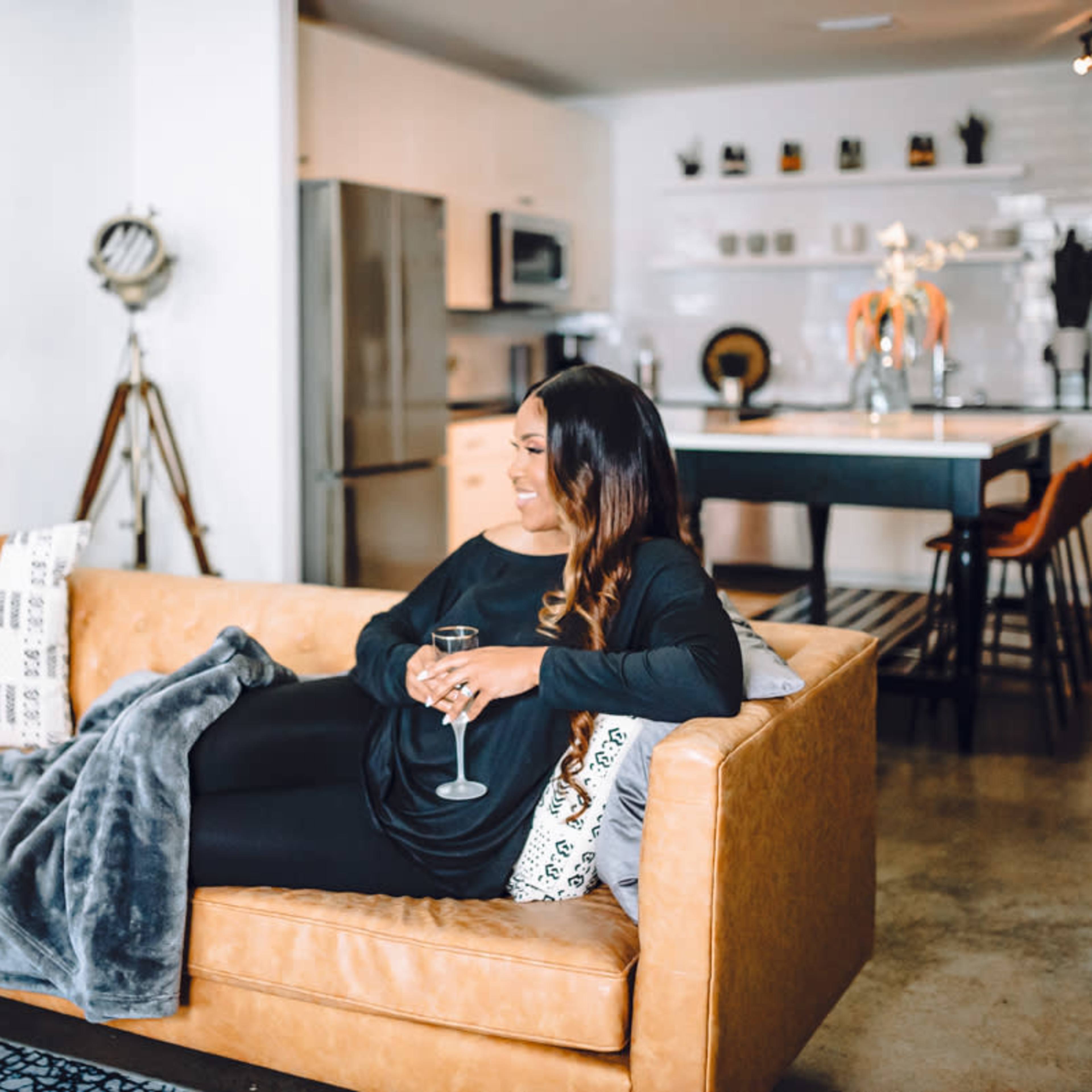 A woman sits on a leather couch in a modern living room, holding a glass of wine, with a cozy blanket draped beside her.