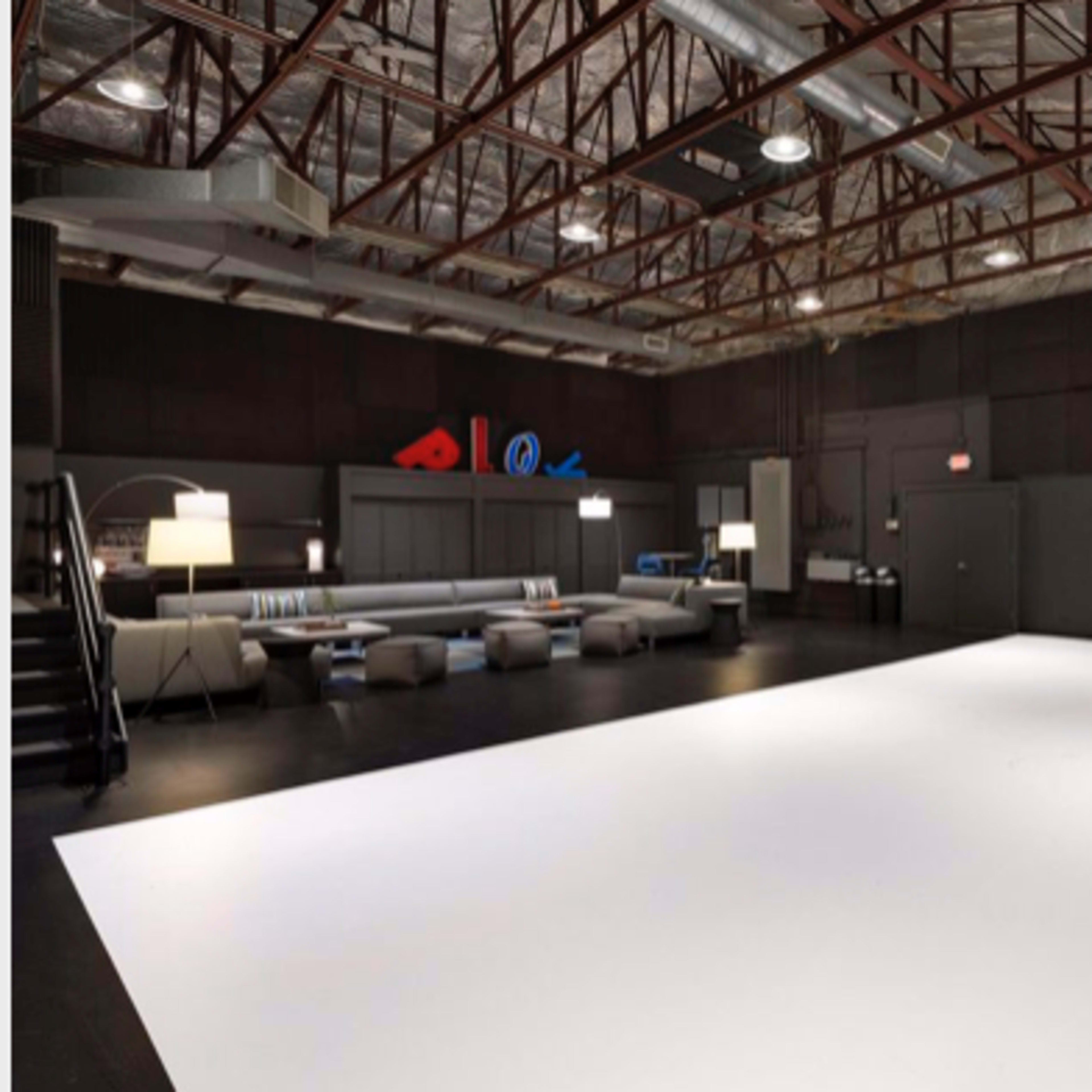 A spacious photography studio with a large white backdrop, modern seating area, and a minimalist table setup.