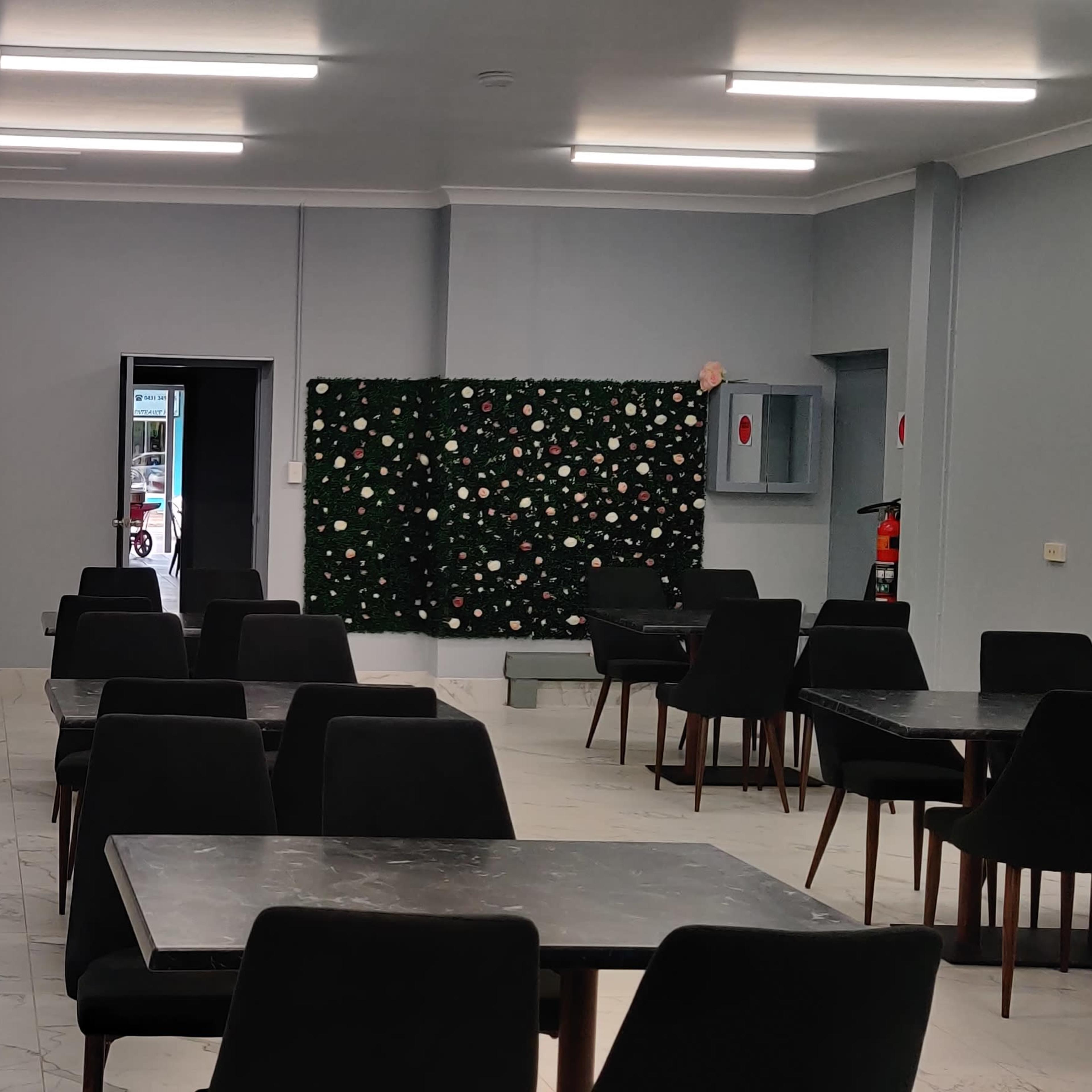 A dining area with several black tables and chairs, large wall mirrors, and green plants on the walls.