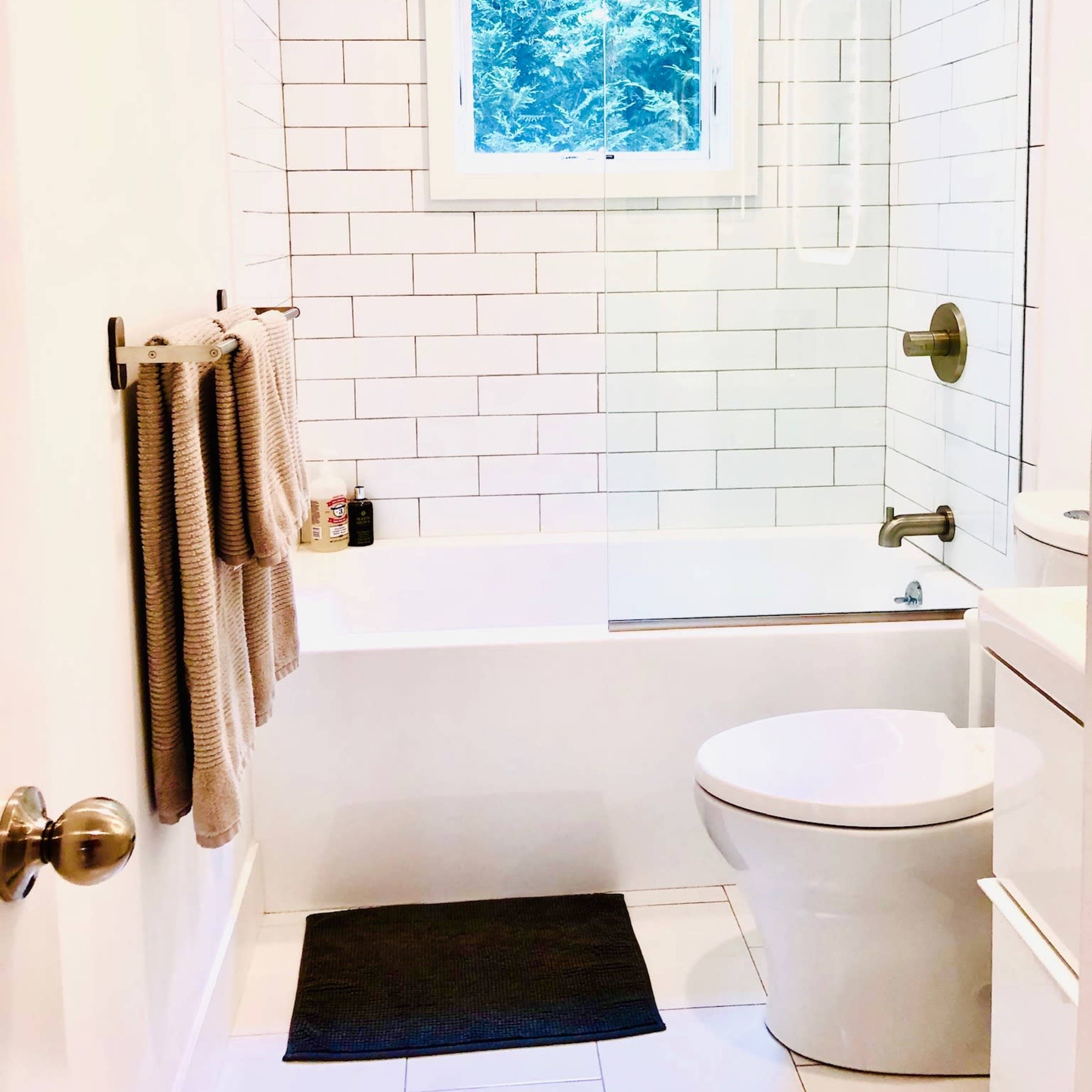 A modern bathroom features a bathtub with a glass shower enclosure, a toilet, and a window that provides natural light.