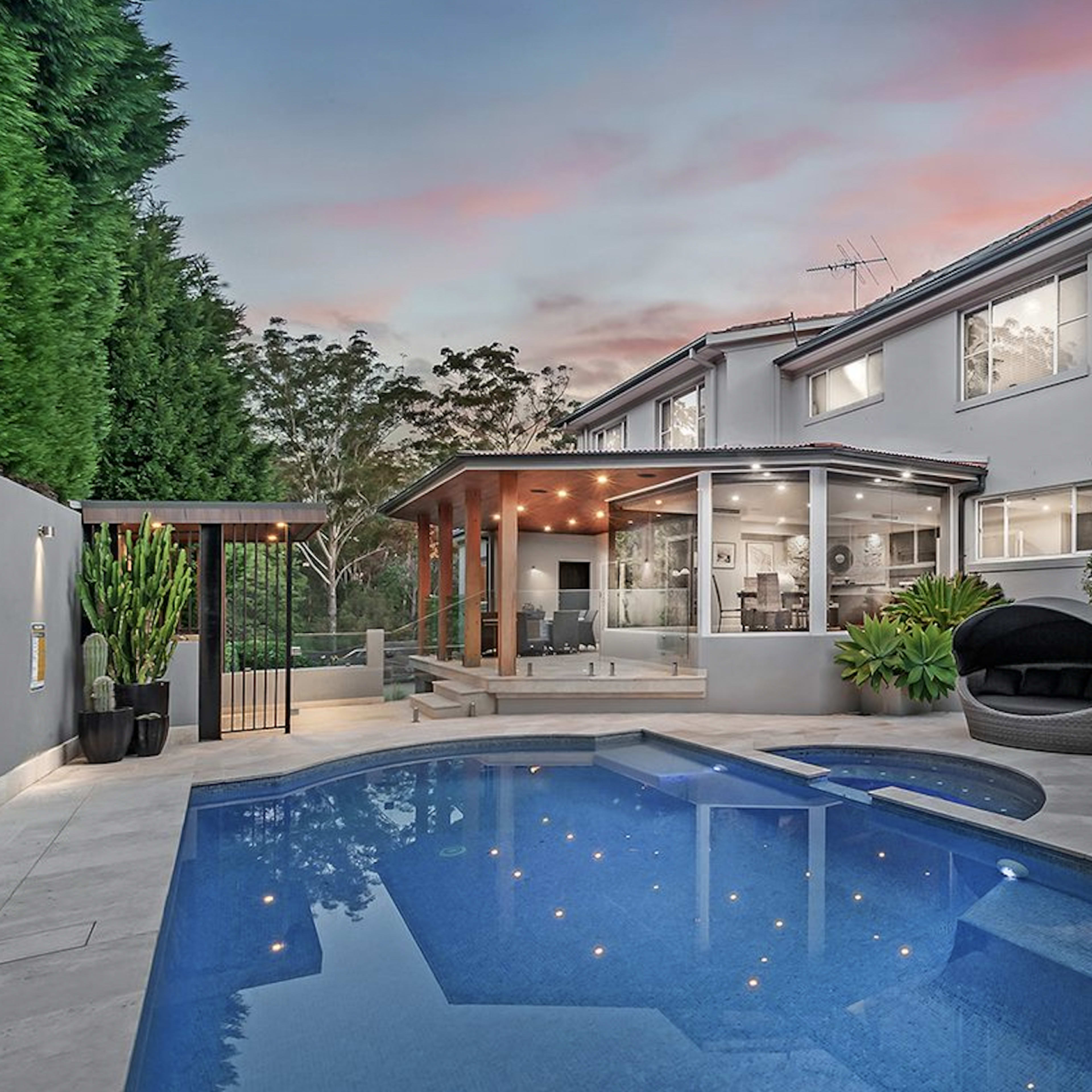 A modern backyard featuring a swimming pool, lounge chairs, and a covered patio adjacent to a two-story house.