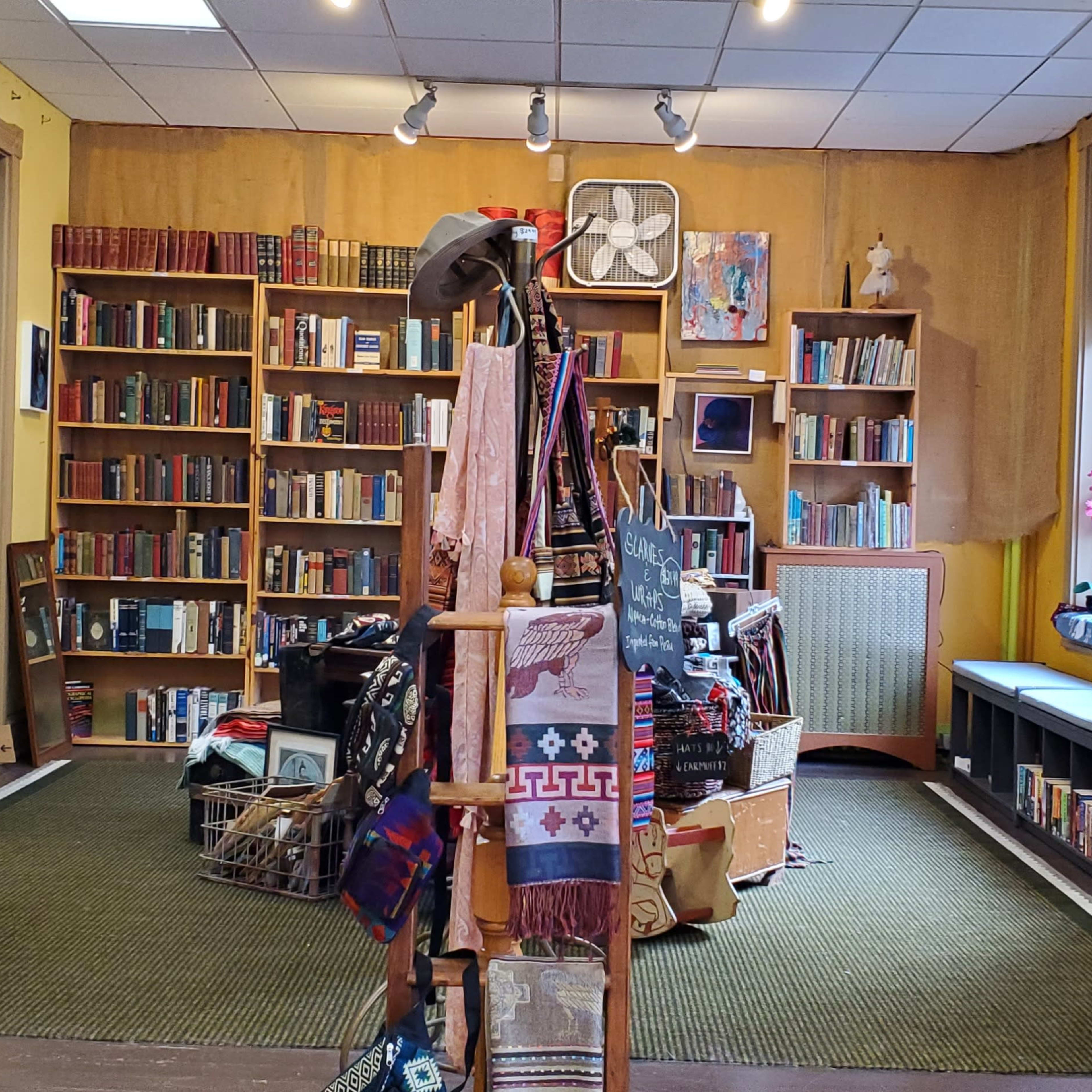 An interior of a bookstore with bookshelves filled with books, artwork on the walls, and a display of scarves and items in the foreground.