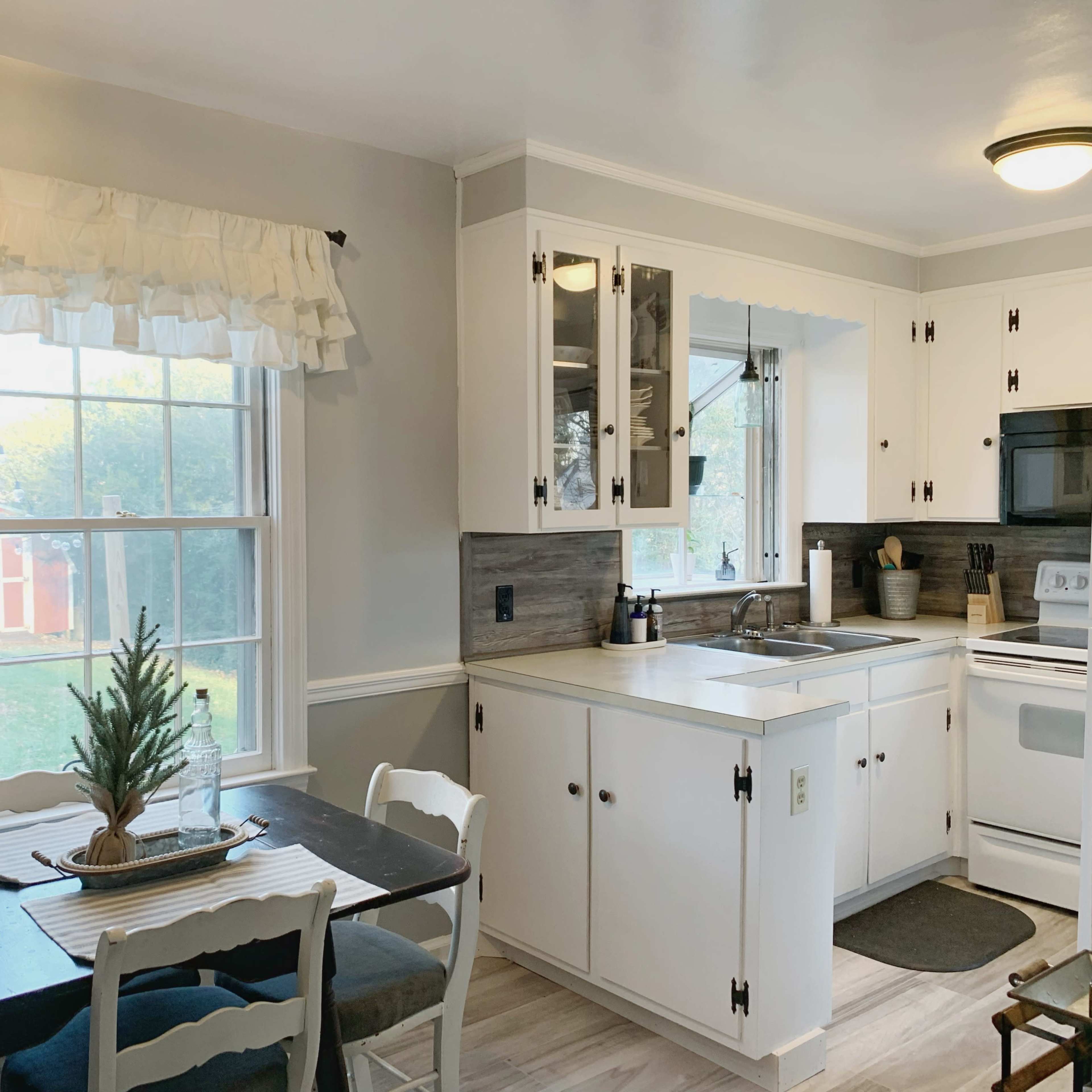 A small kitchen features white cabinetry, a black countertop, and a dining table with chairs by a window.