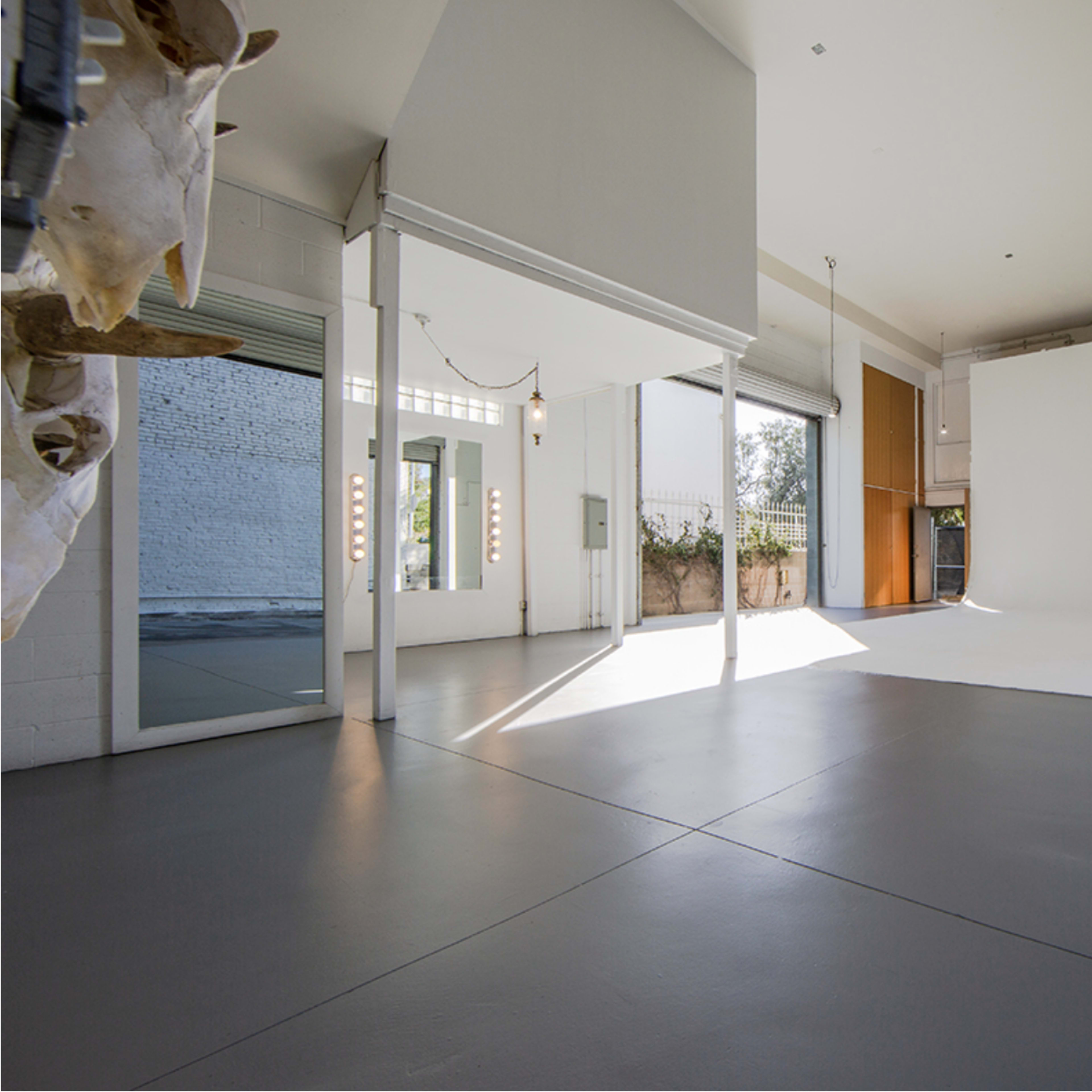 A spacious, empty studio with white walls, large windows, and a gray floor.