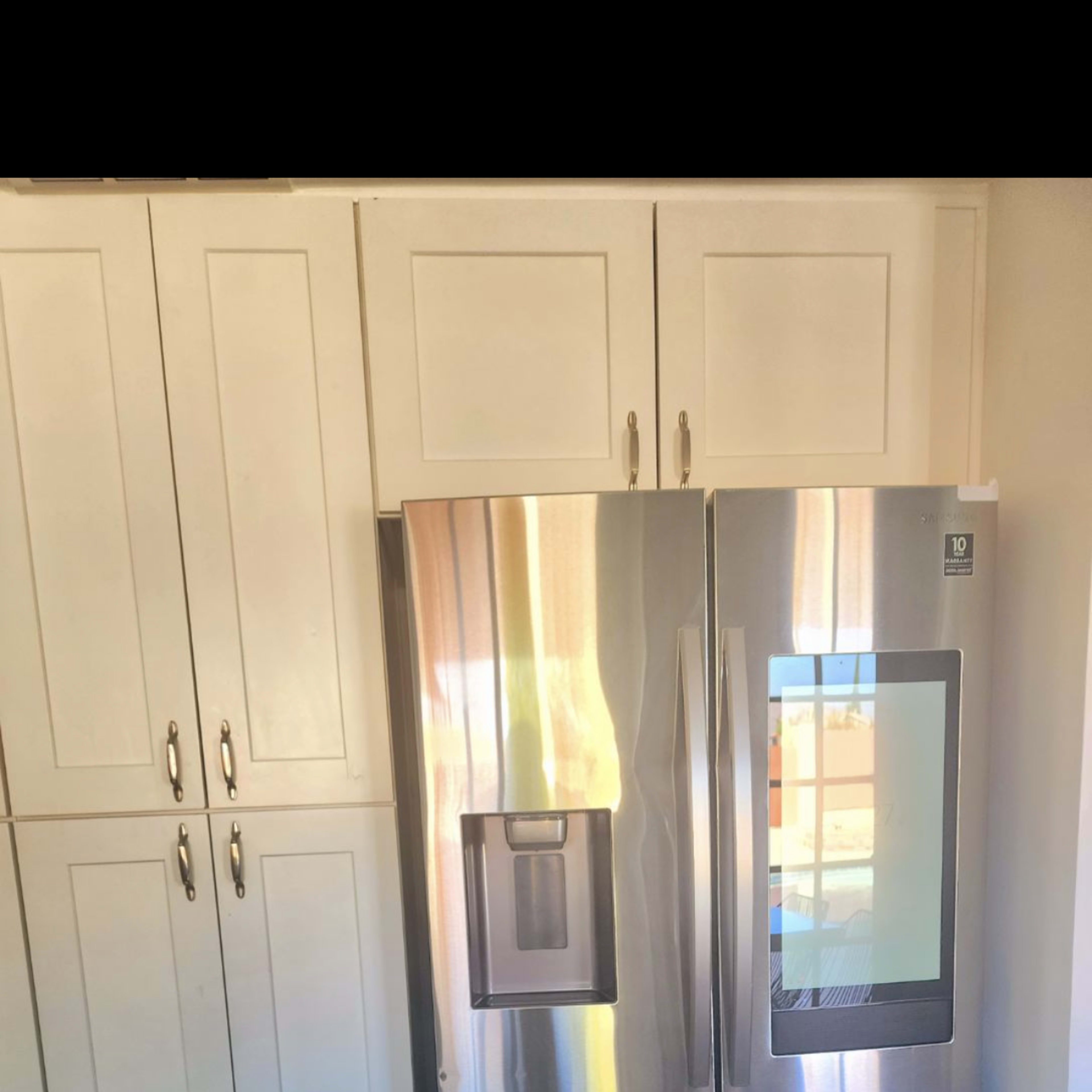 A stainless steel refrigerator positioned between white kitchen cabinets.