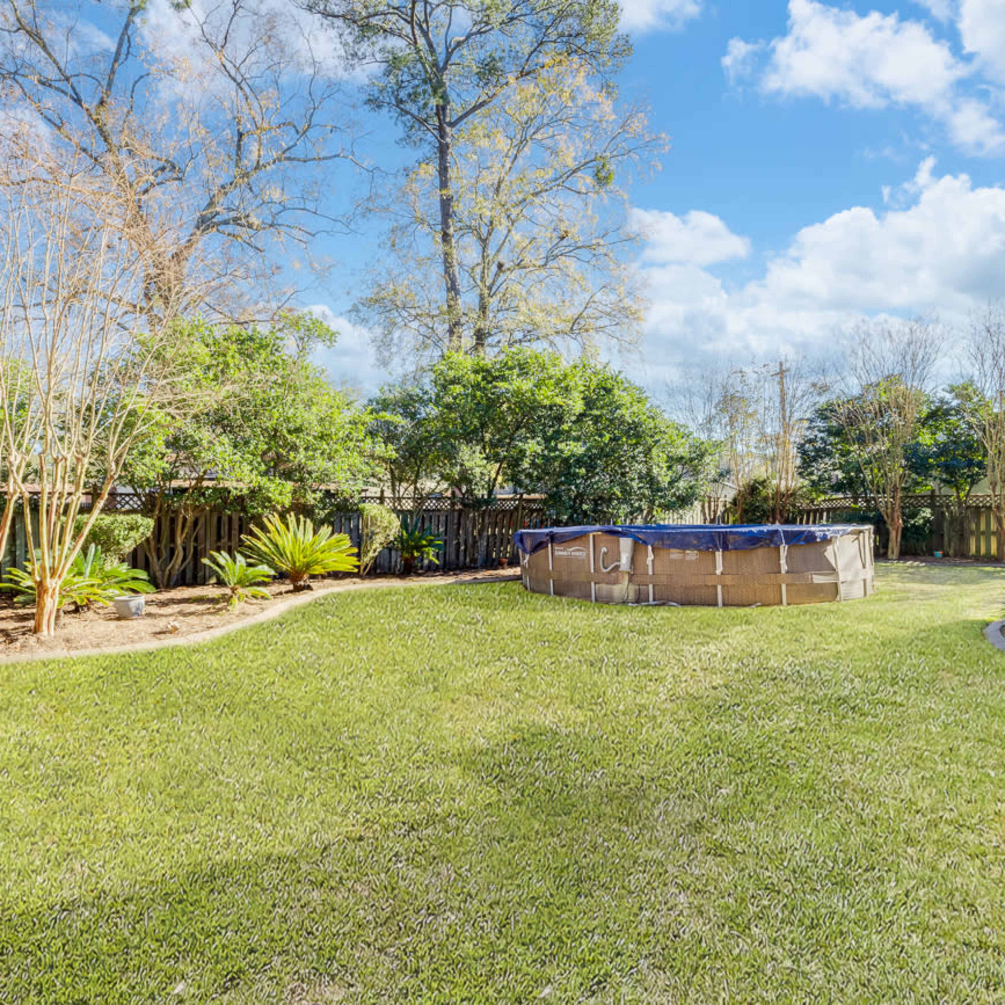 A circular above-ground pool is set in a grassy backyard surrounded by trees and shrubs.