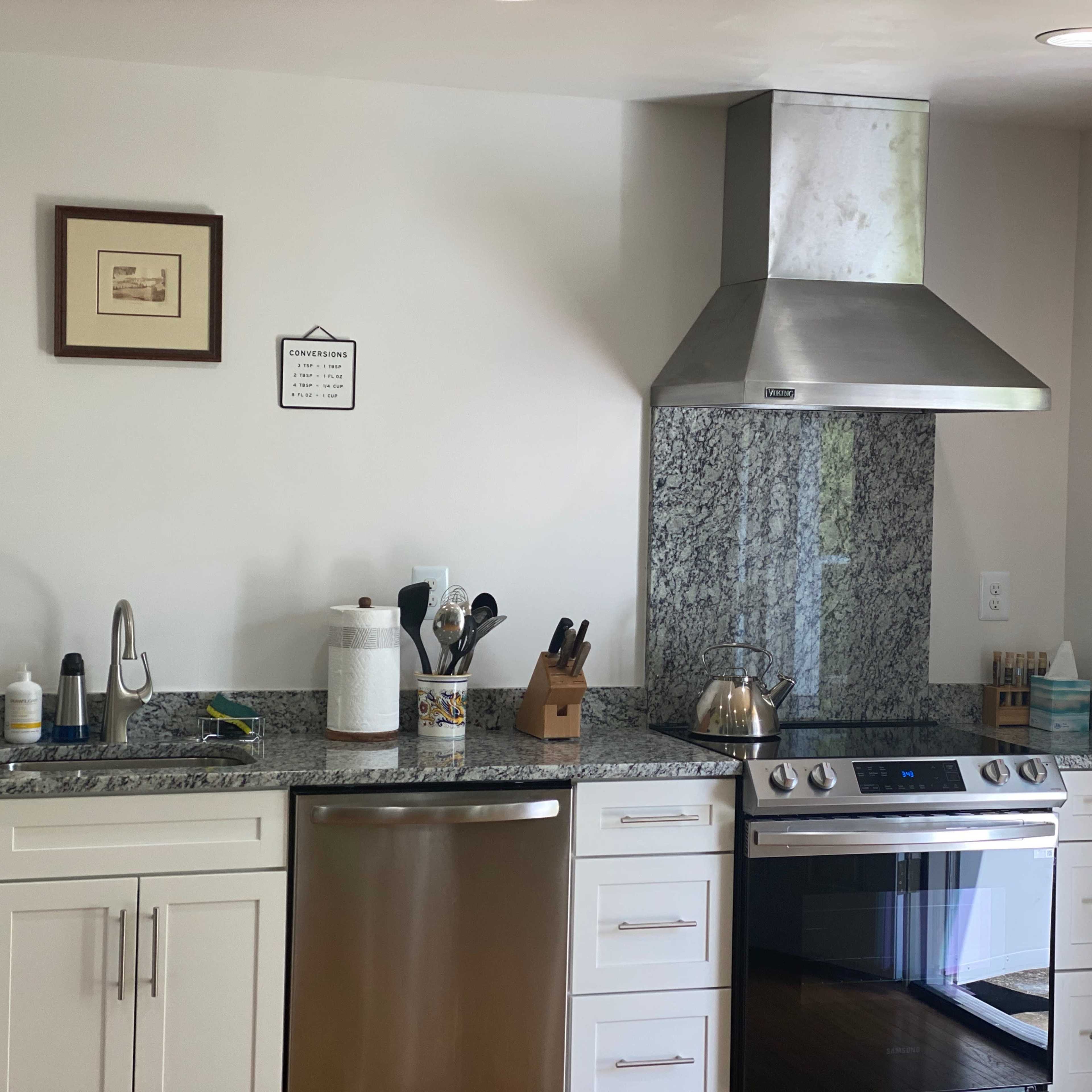 A modern kitchen with silver appliances, a granite countertop, and a stainless steel range hood above the stovetop.
