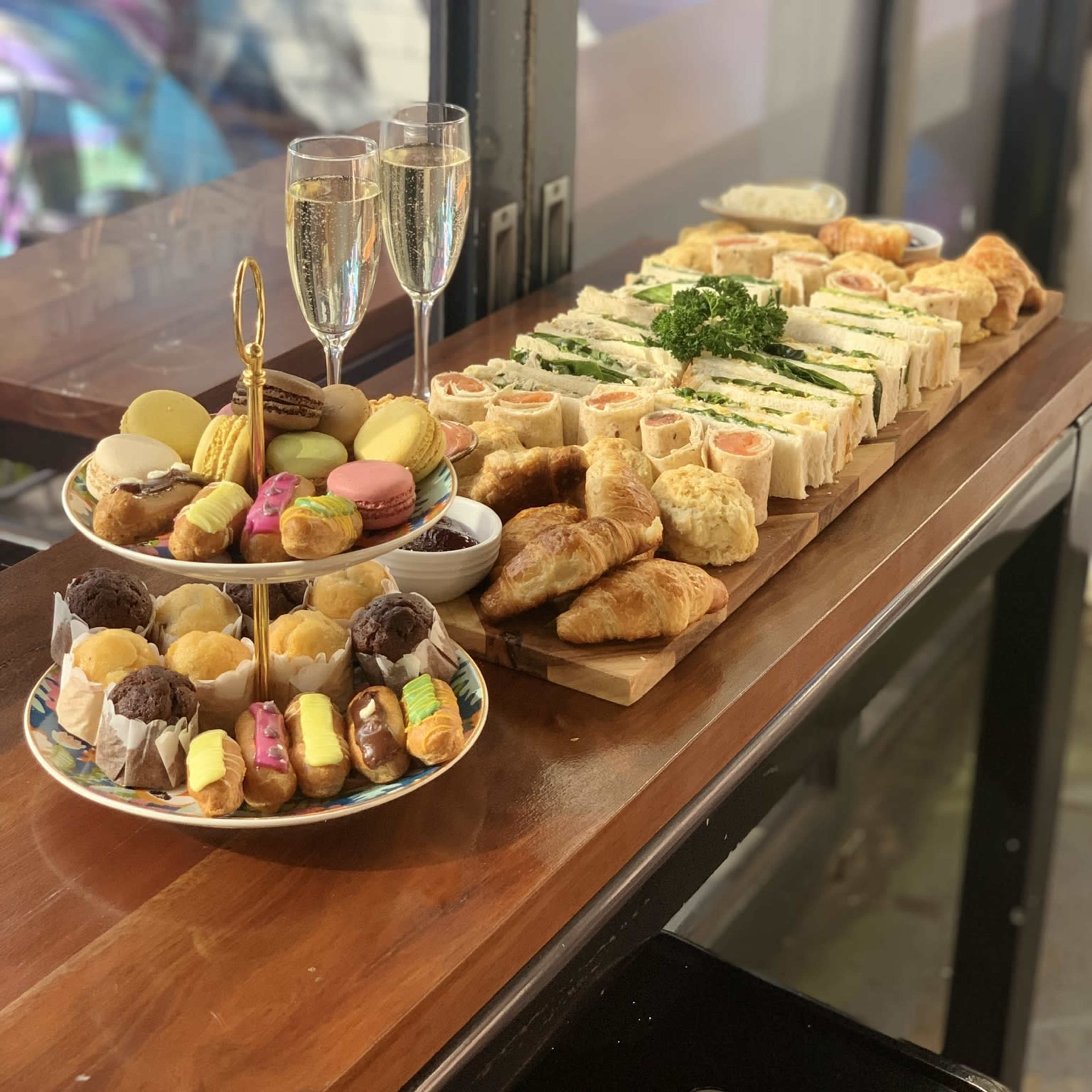 A table displaying an assortment of sandwiches, pastries, and desserts, accompanied by two glasses of champagne.