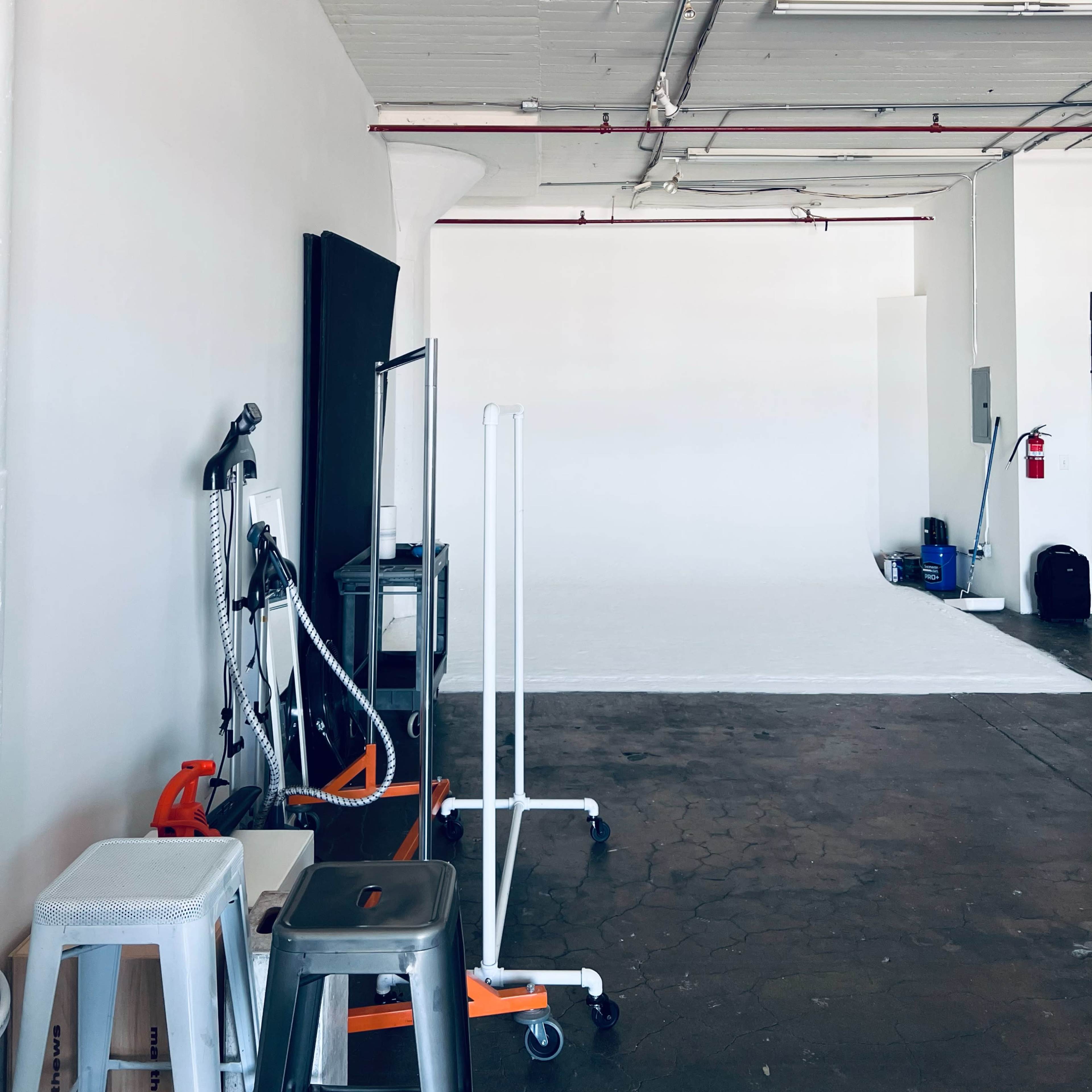 A spacious studio with white walls, exposed ceiling beams, and various equipment on wheels, set against a backdrop of a plain white area.