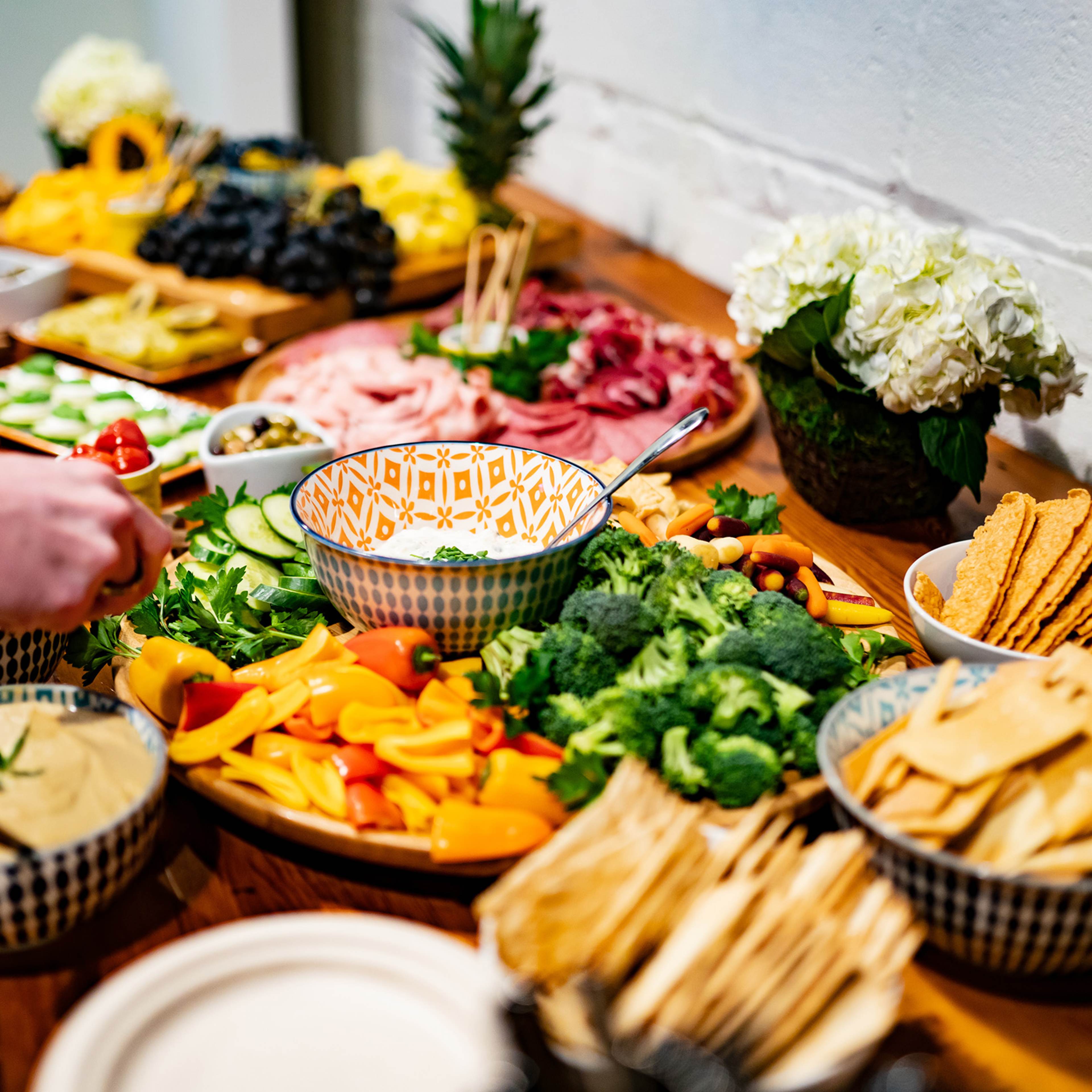 A vibrant spread of various foods, including fruits, vegetables, cheeses, and crackers, is arranged on a wooden table with decorative bowls and platters.