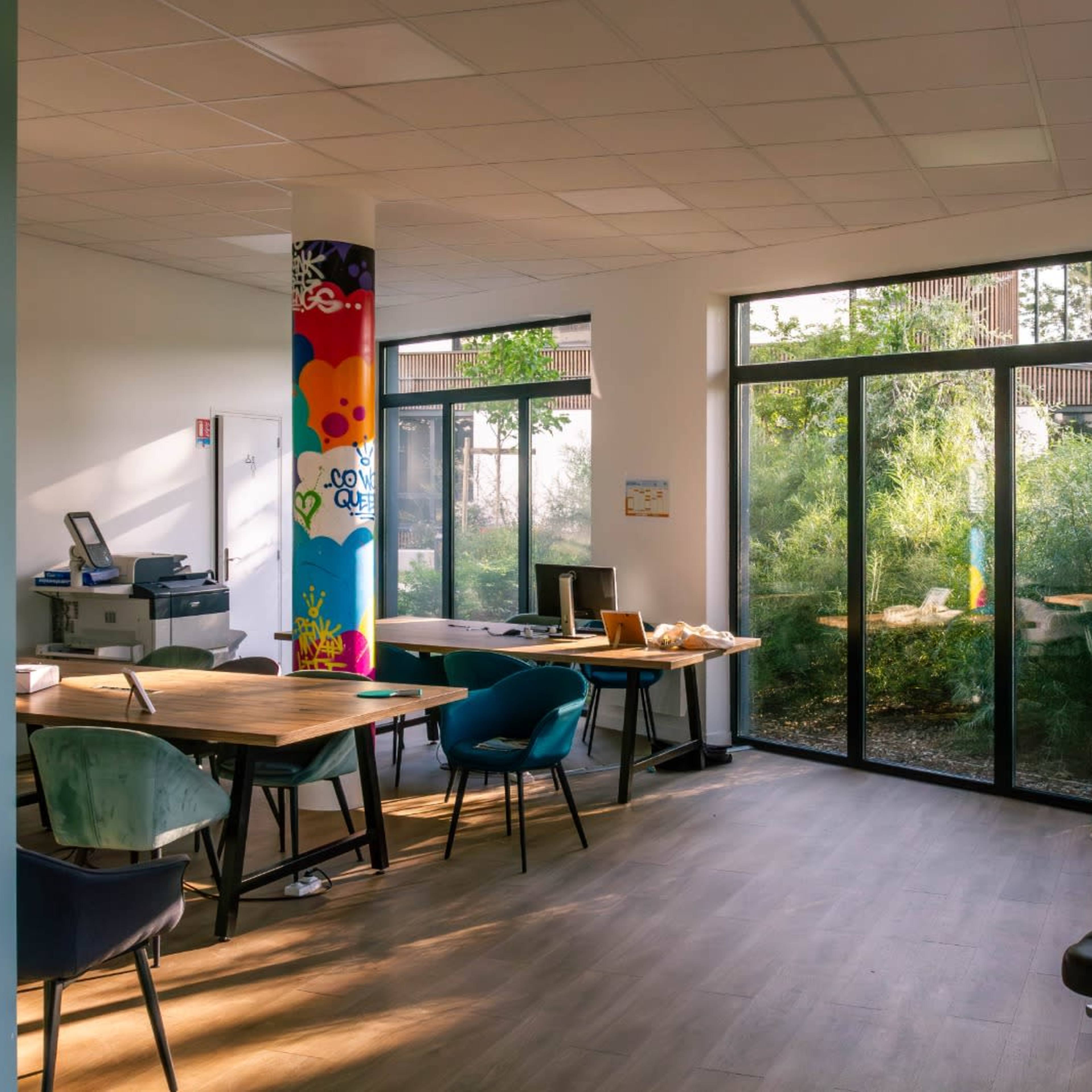 A modern office space featuring large windows, a printer, and colorful pillars adorned with graffiti-style designs.