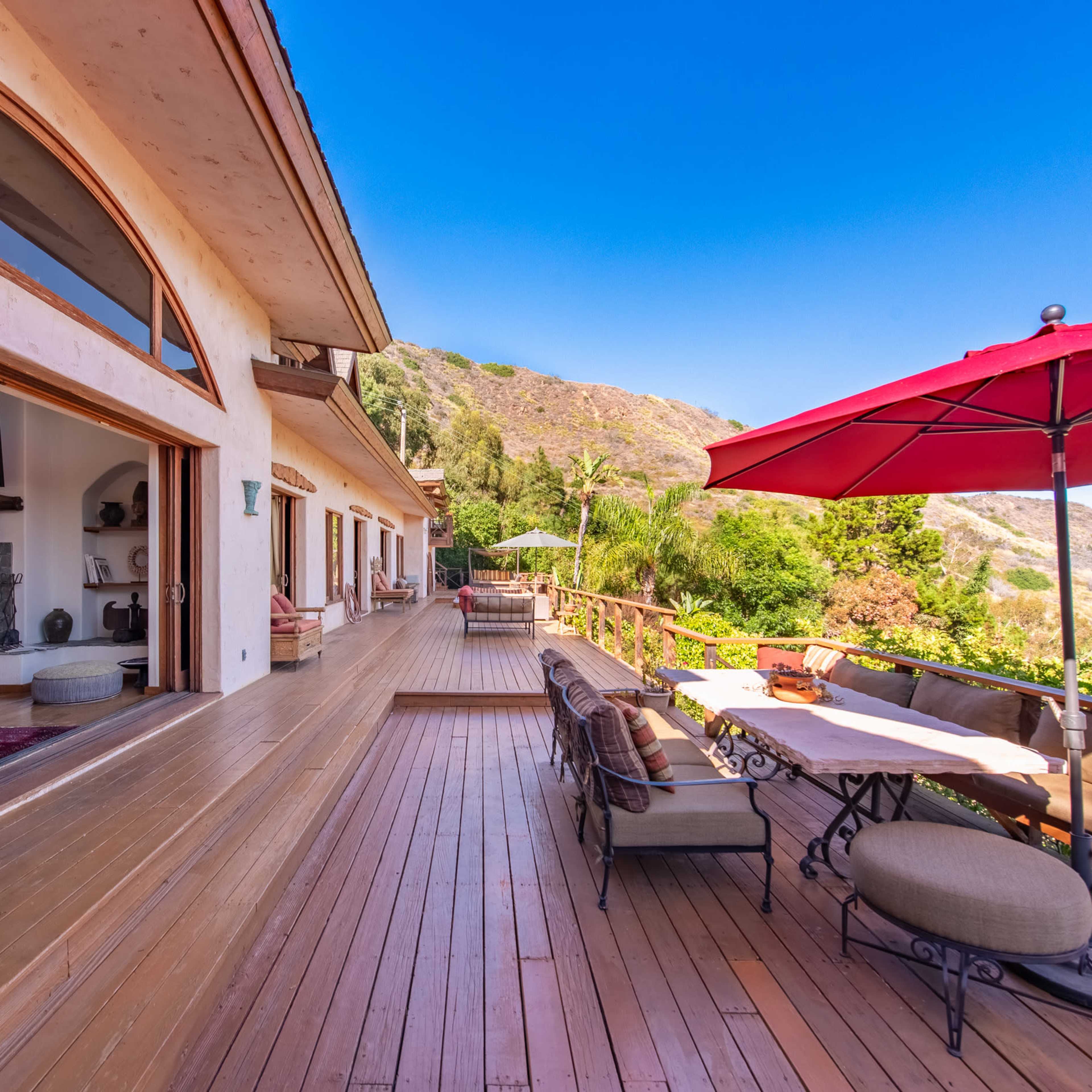 A spacious wooden deck of a house with an outdoor dining area and a view of a hillside landscape.