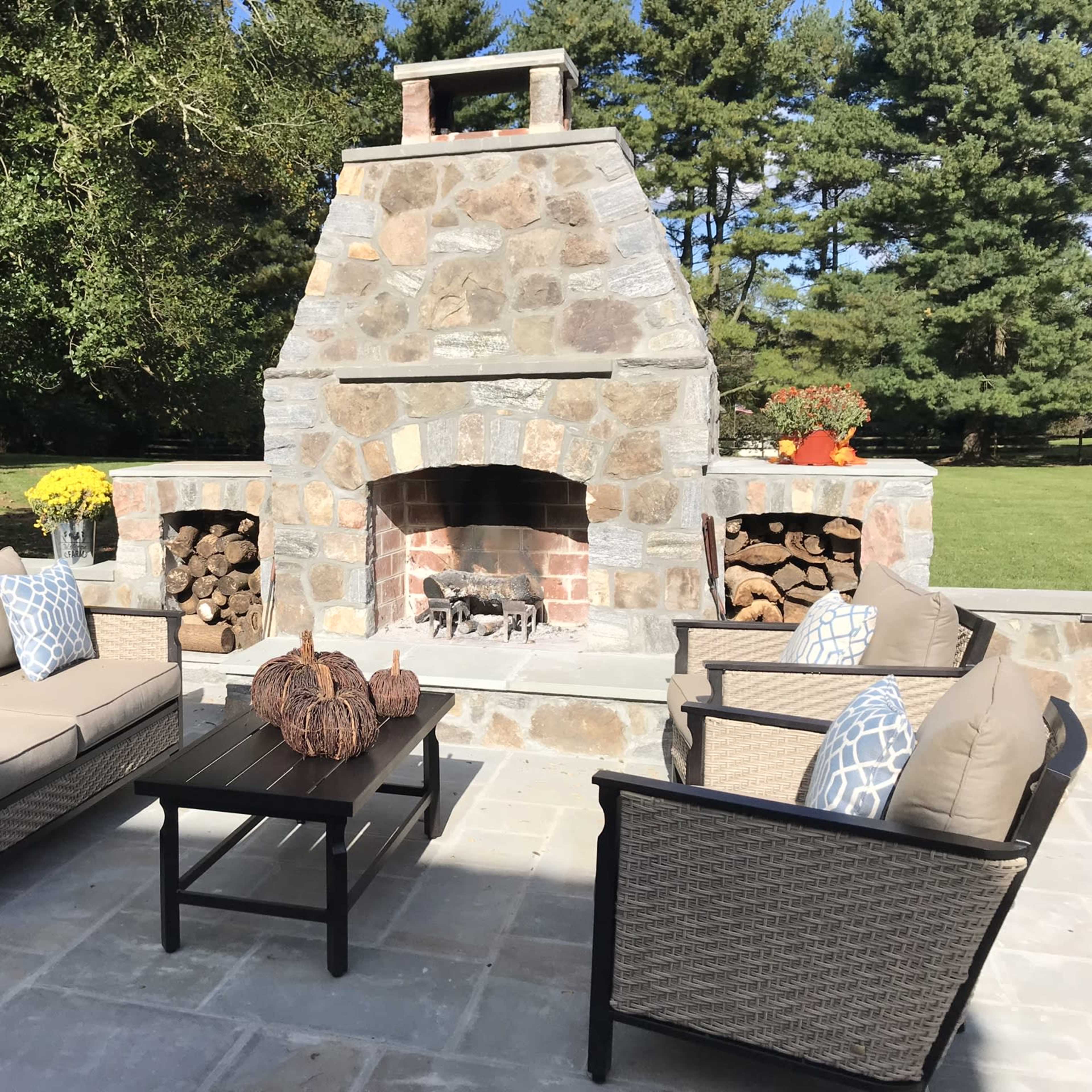 A patio area features a stone fireplace with stacked wood, surrounded by seating arrangements and a coffee table.