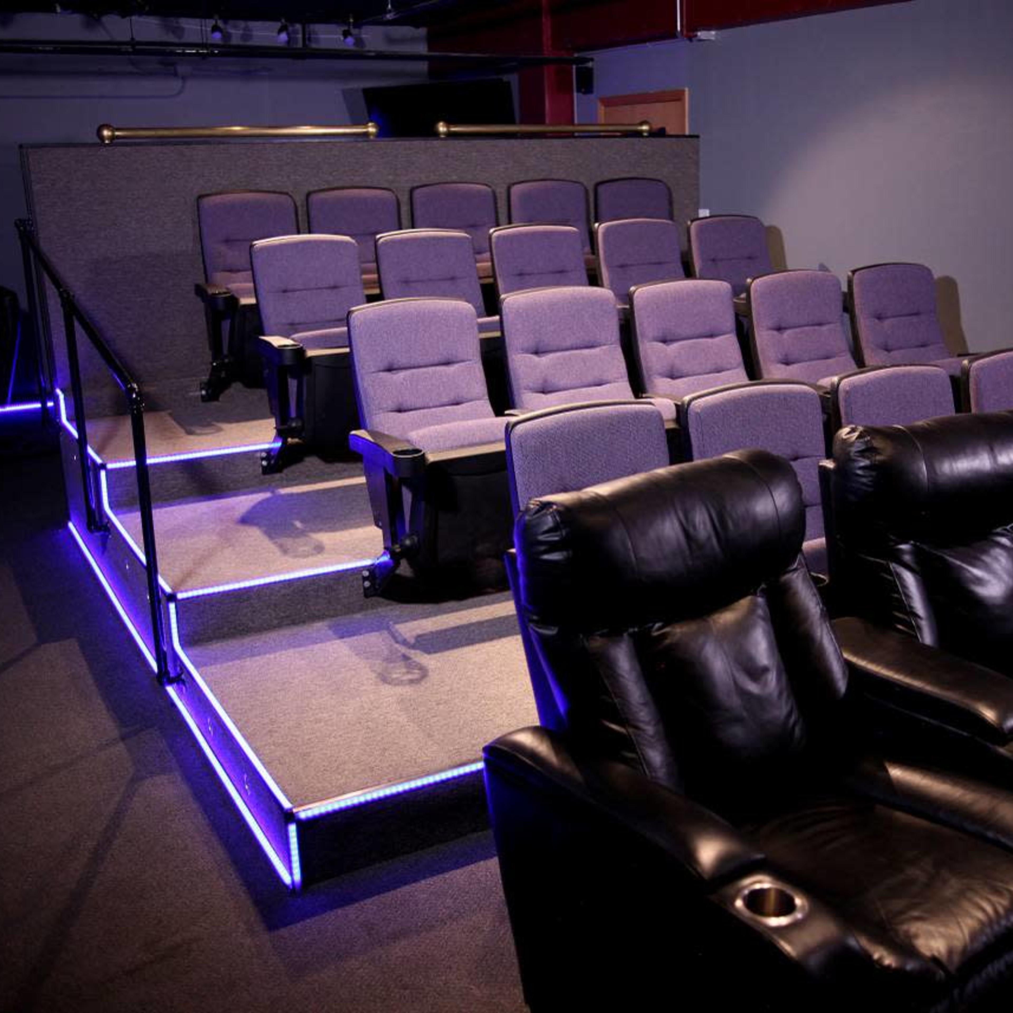 A small home theater with tiered seating comprising gray chairs and black recliners, illuminated by blue LED lights.